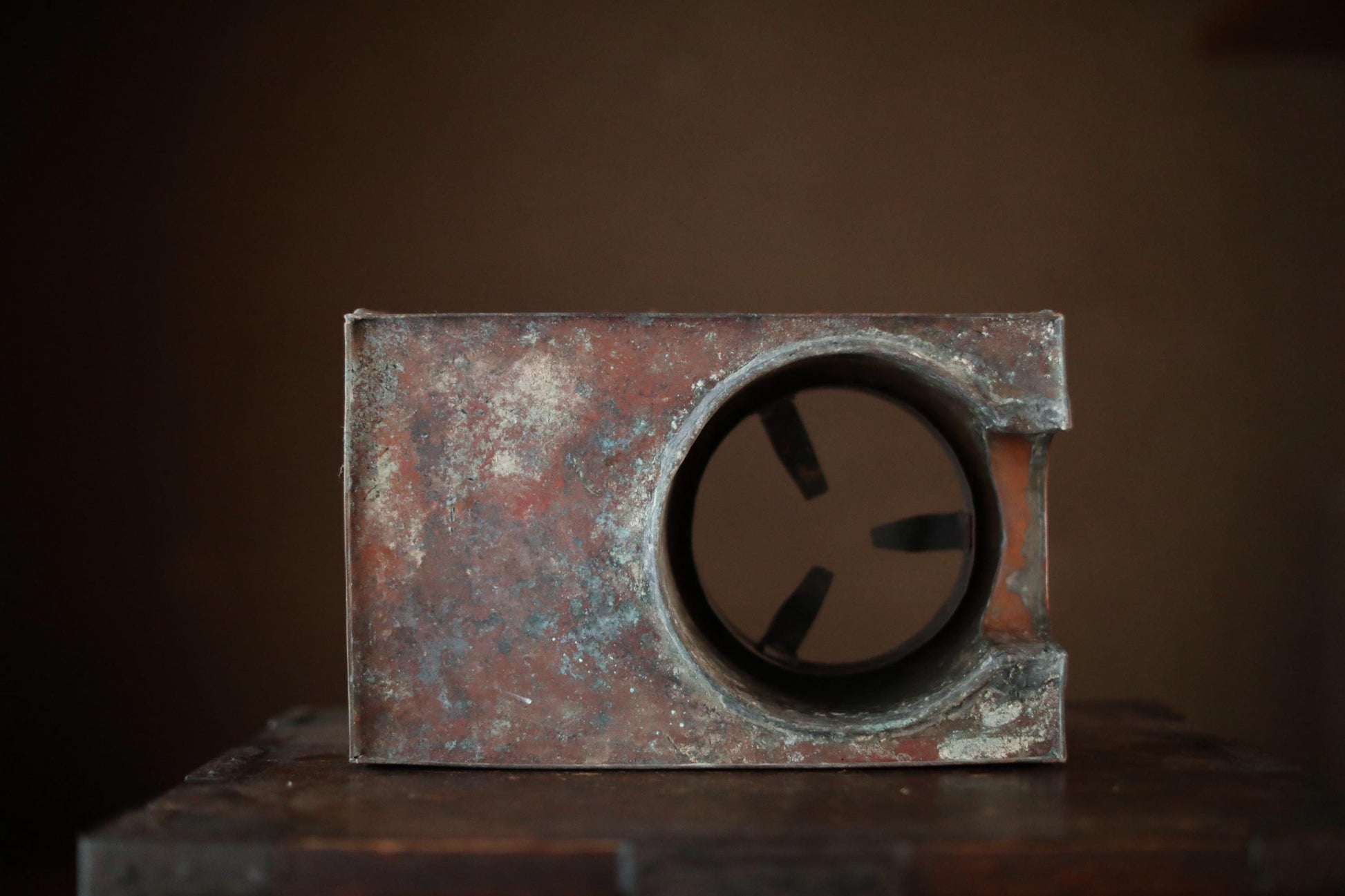 a rusted metal object with a circular opening, sitting on a wooden surface against a dark background.