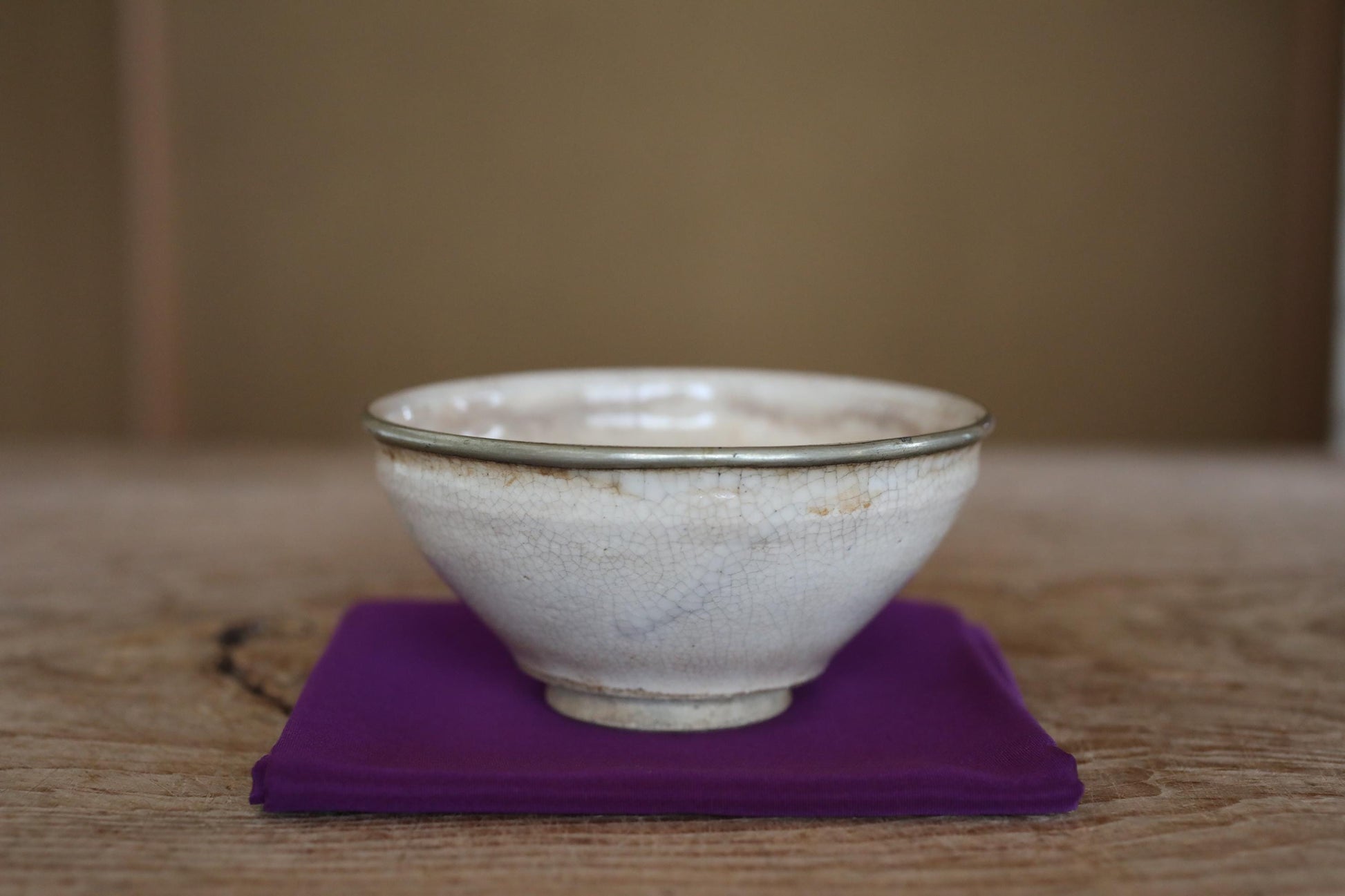 A white ceramic bowl with a silver rim sits on a purple cloth on a wooden surface.