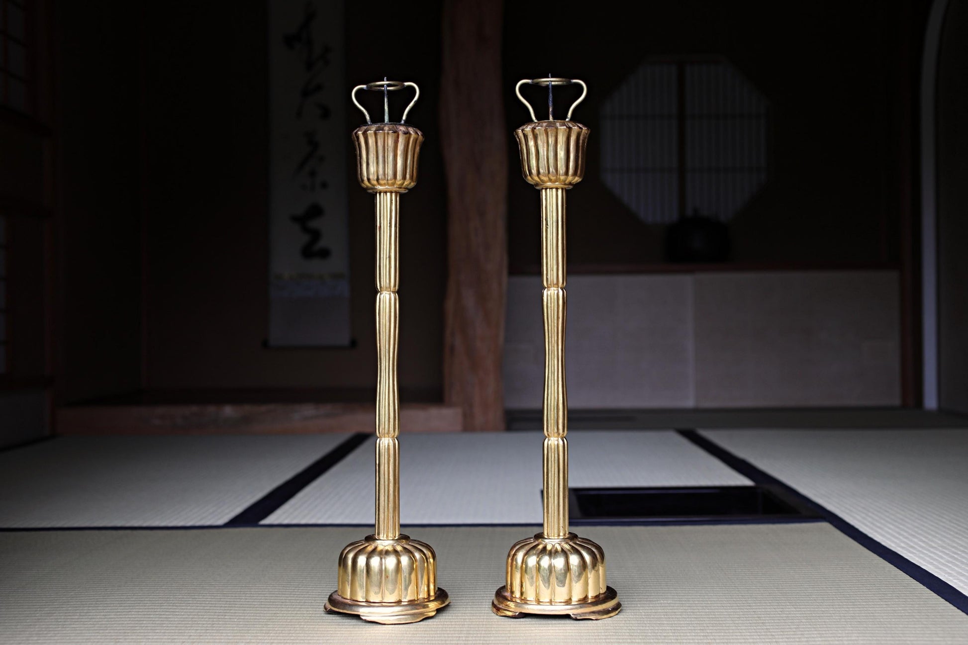 two golden candlesticks standing side by side on a tatami mat.