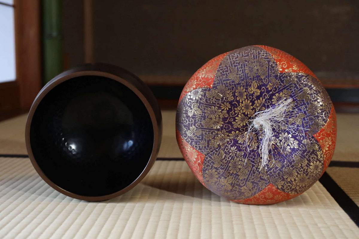 two decorative bowls, one with a black interior and the other with a colorful, patterned interior, placed on a tatami mat.