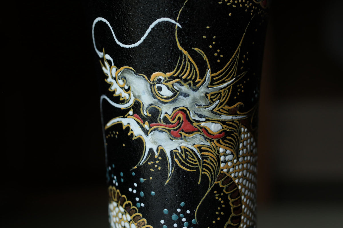 a close-up view of a black vase with a detailed dragon design painted on it.