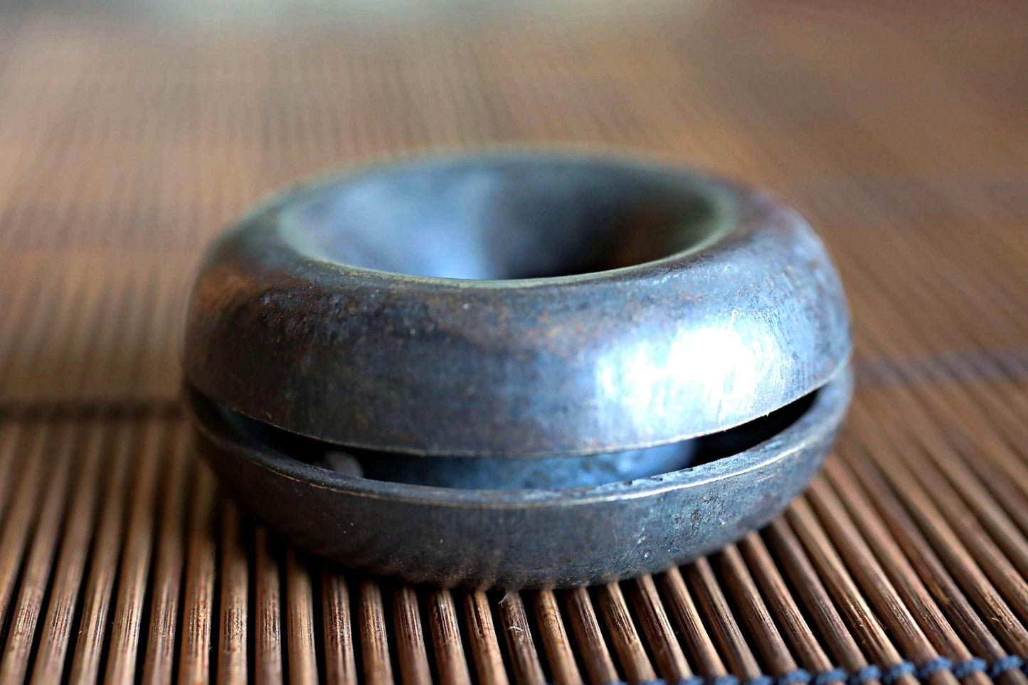 A close-up image of a metal object, possibly a small bowl or container, resting on a bamboo mat or placemat.