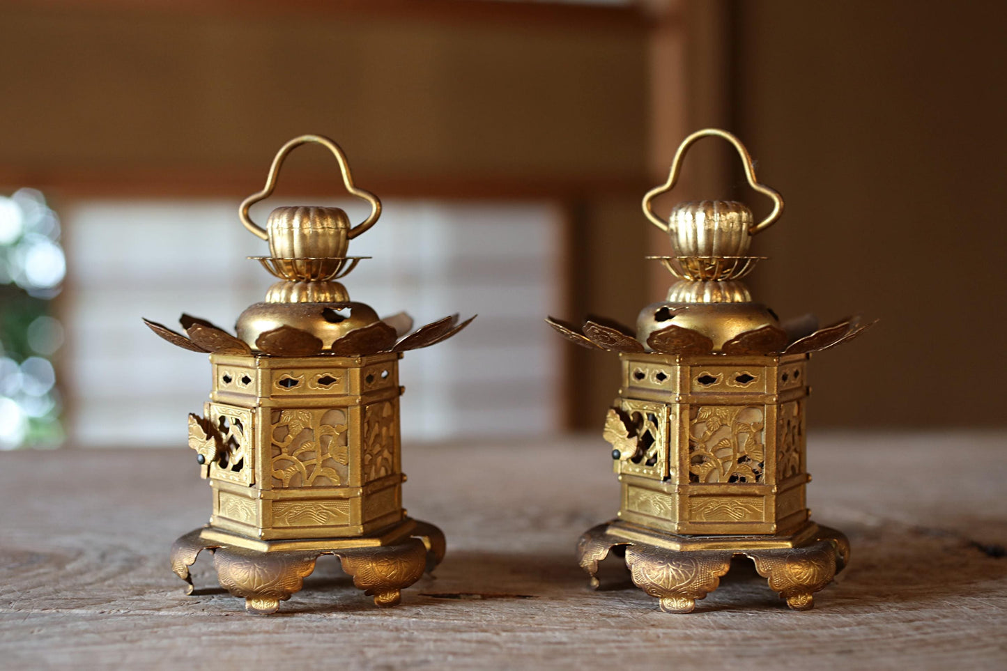 Two ornate golden lanterns with intricate designs and handles, placed on a wooden surface.