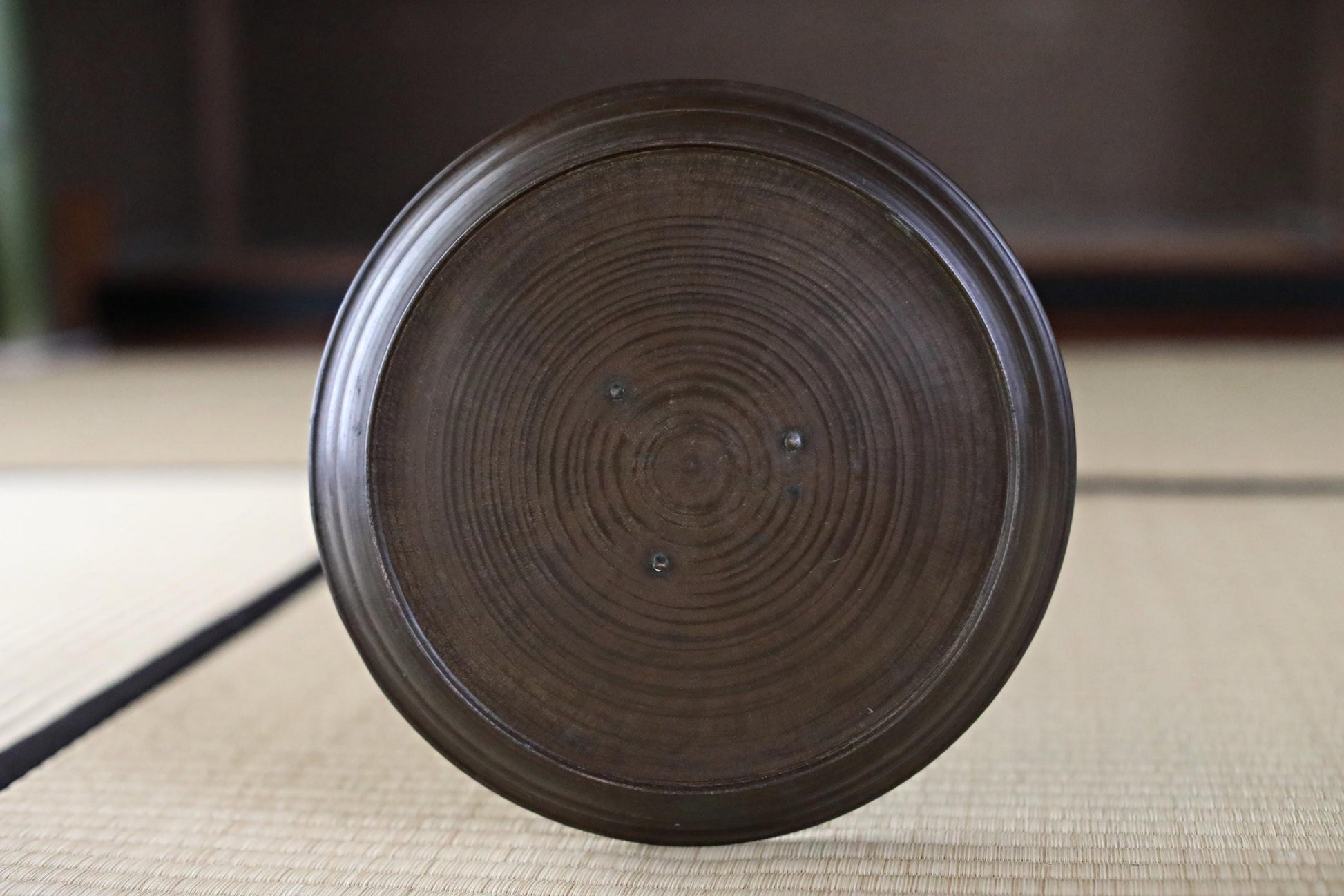 A dark brown, circular plate or bowl with a textured surface, placed on a woven mat or mat-like surface.