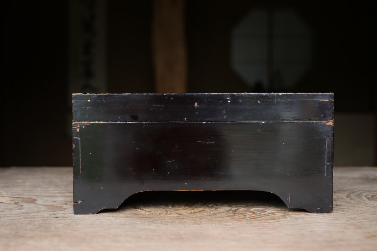 A black wooden box with a flat top sits on a wooden surface.