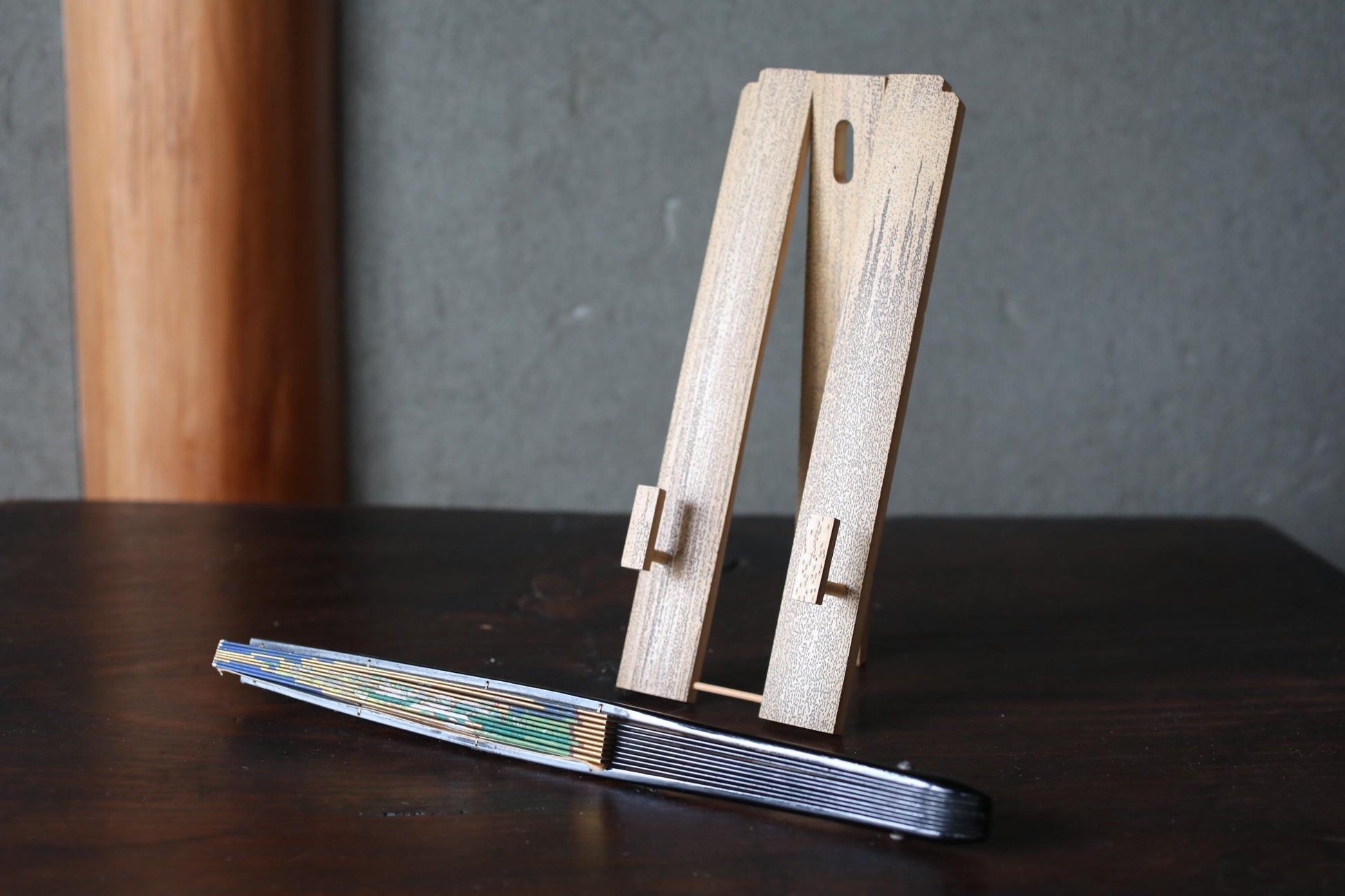 a wooden stand with two vertical slats and a horizontal slat, placed on a dark wooden surface. Next to the stand, there is a metal object with a striped pattern.