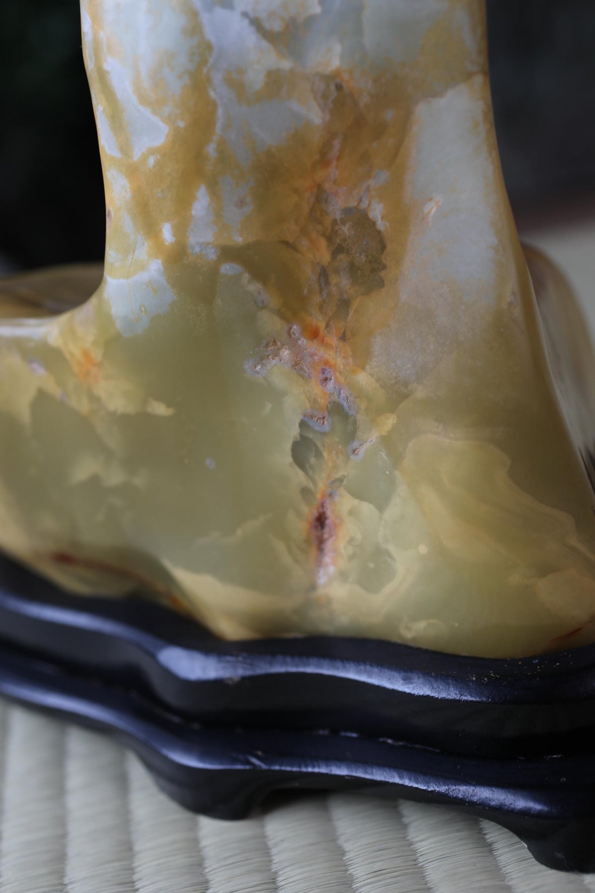 a close-up view of a yellowish-green stone or rock with a rough, textured surface. The stone appears to be a type of stone or rock, possibly a type of marble or slate. The stone is placed on a black stand or base, which contrasts with the stone's color and texture. The image does not contain any other objects or text.