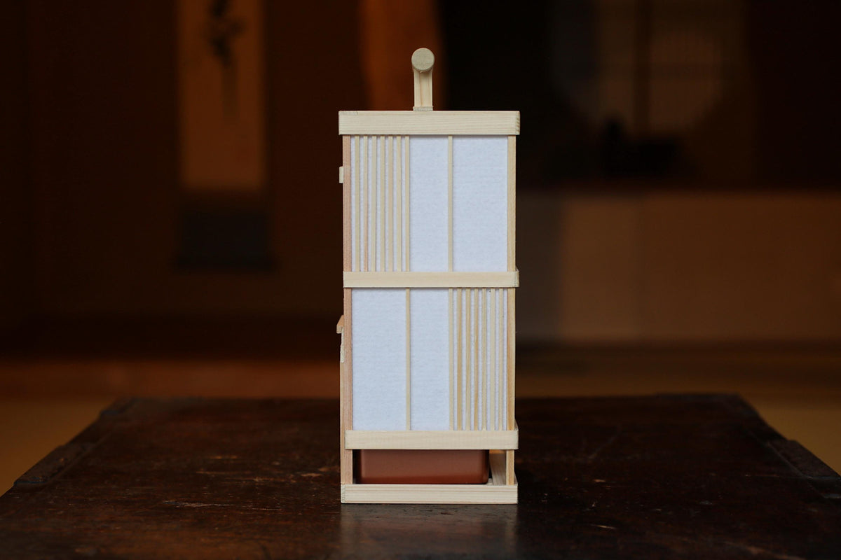 A wooden lantern with a white paper covering is displayed on a dark wooden surface.