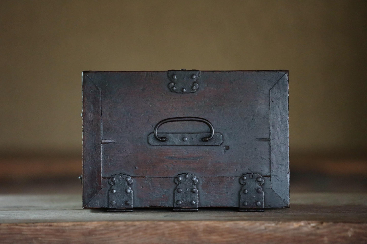 A dark wooden chest with metal clasps and handles sits on a wooden surface.