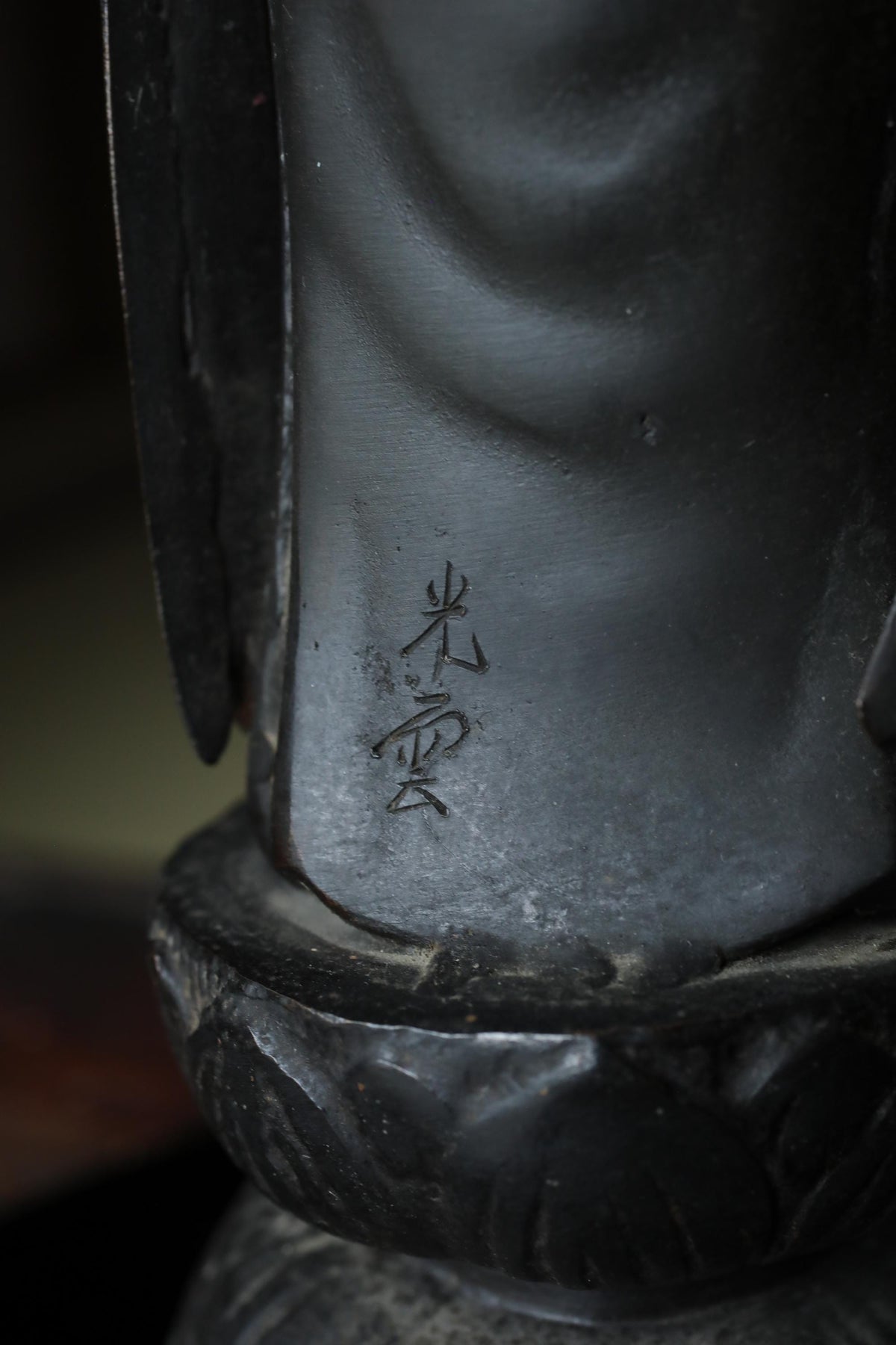A close-up view of a dark-colored metal object, possibly a sculpture or a piece of art, with an Asian-style symbol or text engraved on its surface.