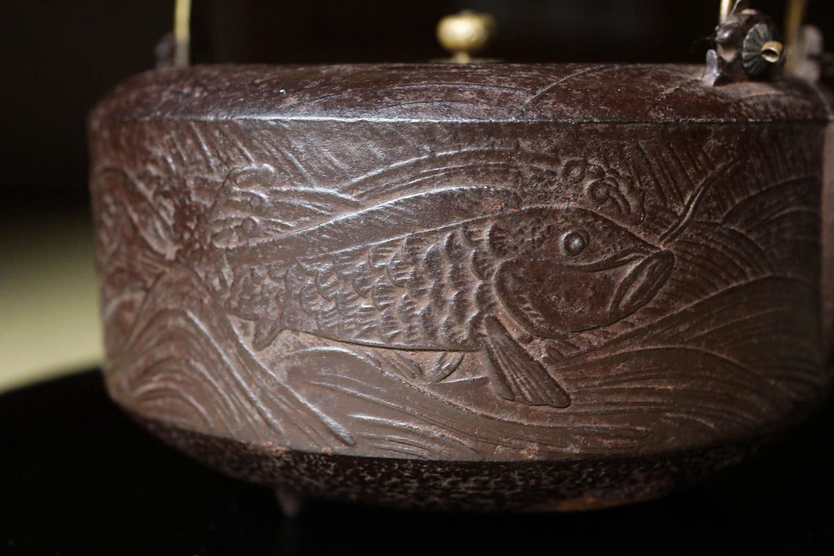 A close-up image of a decorative metal object, possibly a piece of pottery or a sculpture, featuring an embossed fish design.