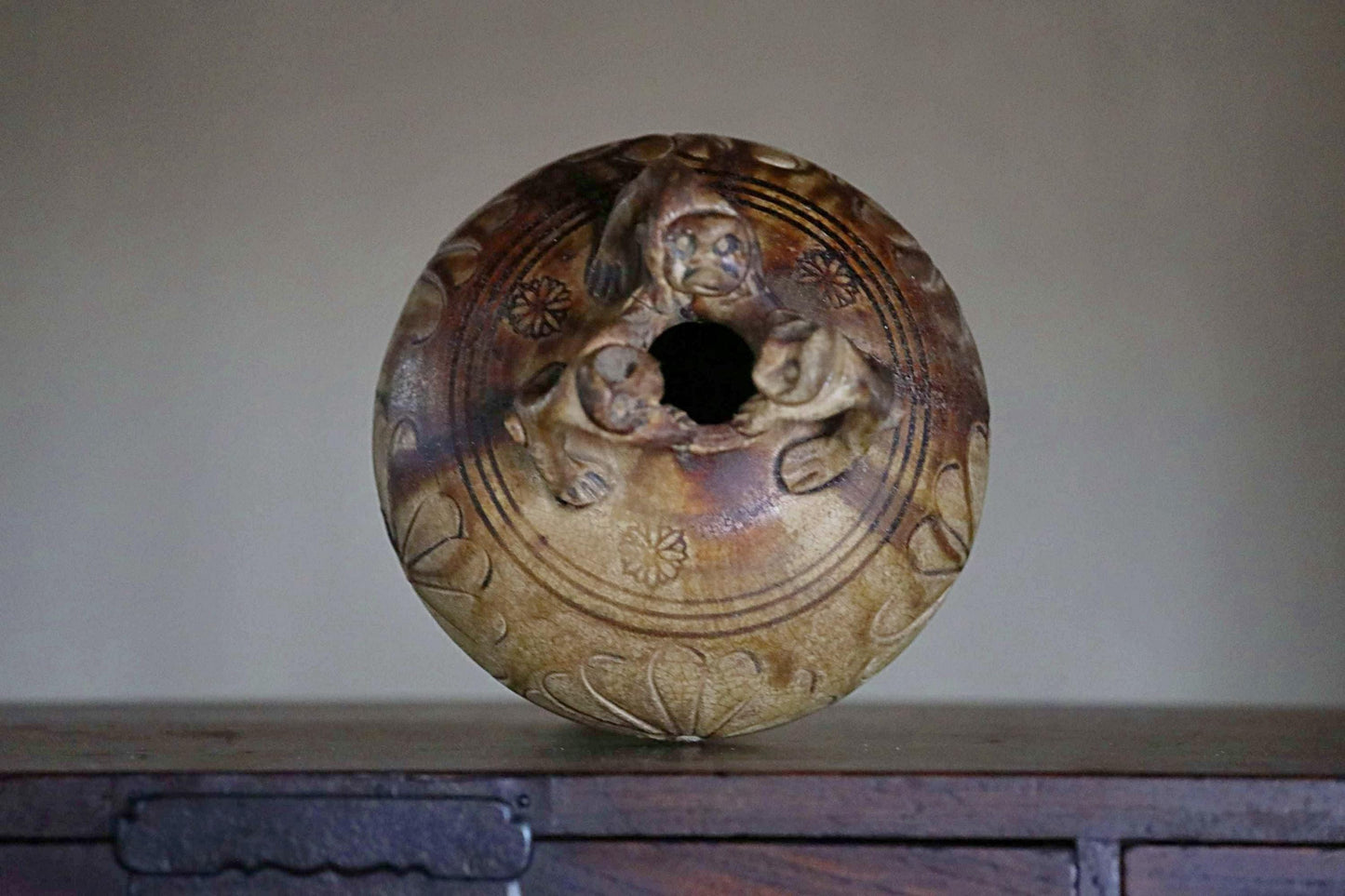 A ceramic vase with intricate designs and a central hole, sitting on a wooden surface.