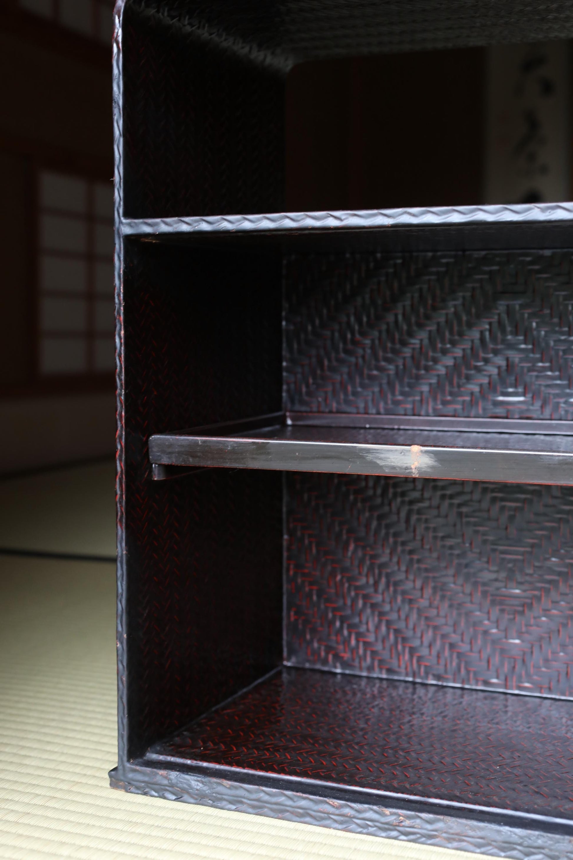 a close-up view of a dark-colored metal shelf or cabinet with a woven texture.