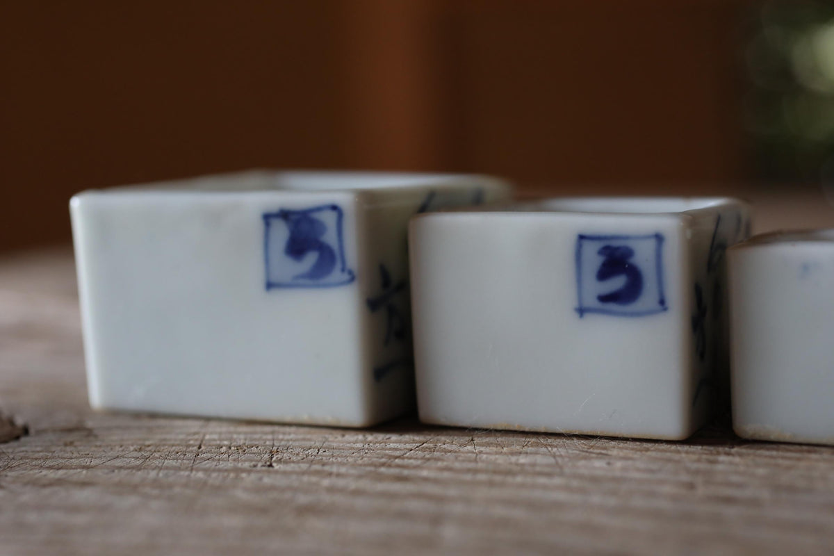 a close-up view of three white ceramic containers with blue markings on them, placed on a wooden surface.