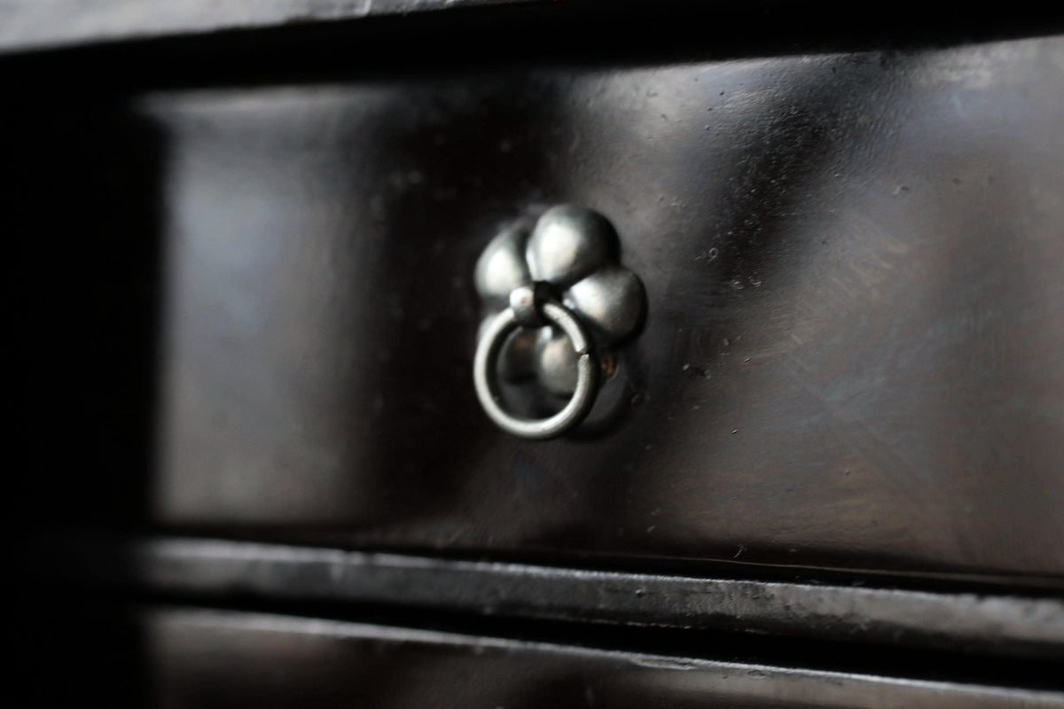 A close-up view of a metal drawer pull with a floral design on a dark wooden surface.