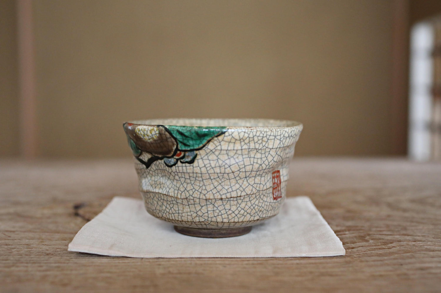 A ceramic cup with a green and white design sits on a white napkin on a wooden table.