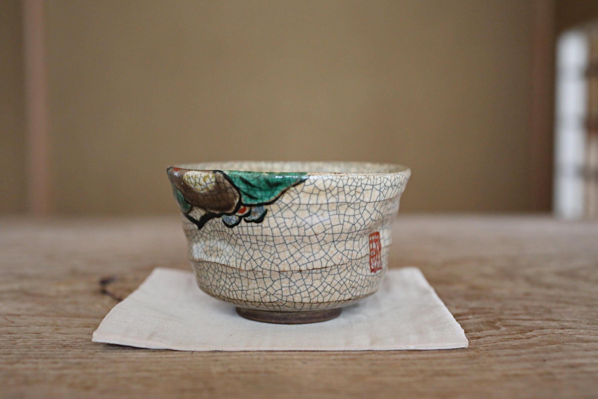 A ceramic cup with a green and white design sits on a white napkin on a wooden table.