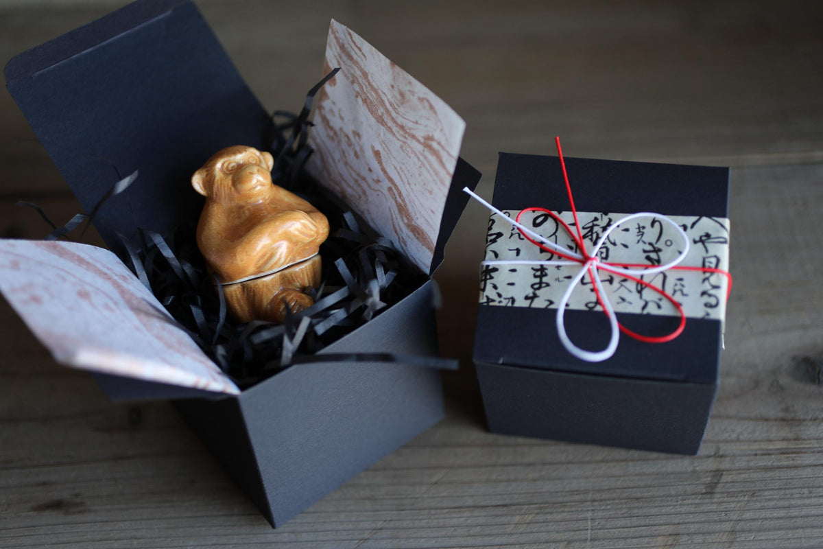 a small brown figurine sitting inside a black box, which is placed on a wooden surface.