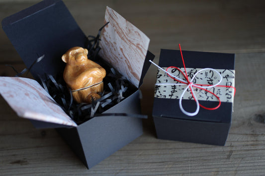 a small brown figurine sitting inside a black box, which is placed on a wooden surface.