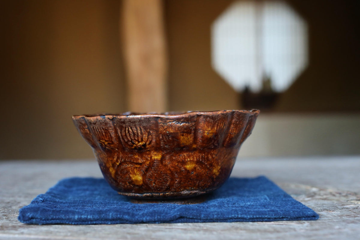 A brown ceramic bowl with a scalloped edge sits on a blue cloth on a wooden surface.