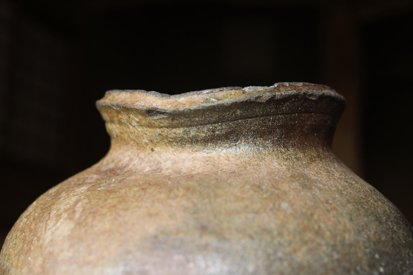 A close-up view of an old, weathered clay pot with a rough, textured surface.