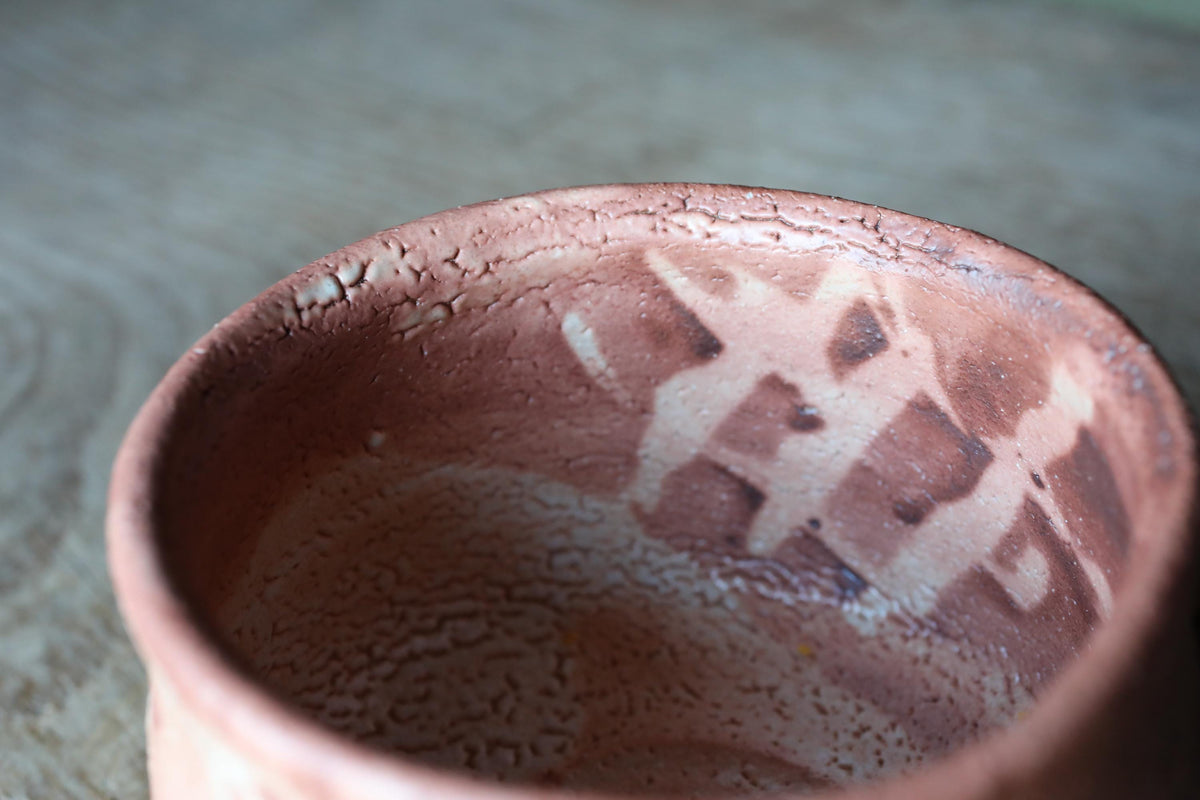 A close-up image of a clay bowl with a textured surface, featuring a pattern of small lines or dots on the surface.