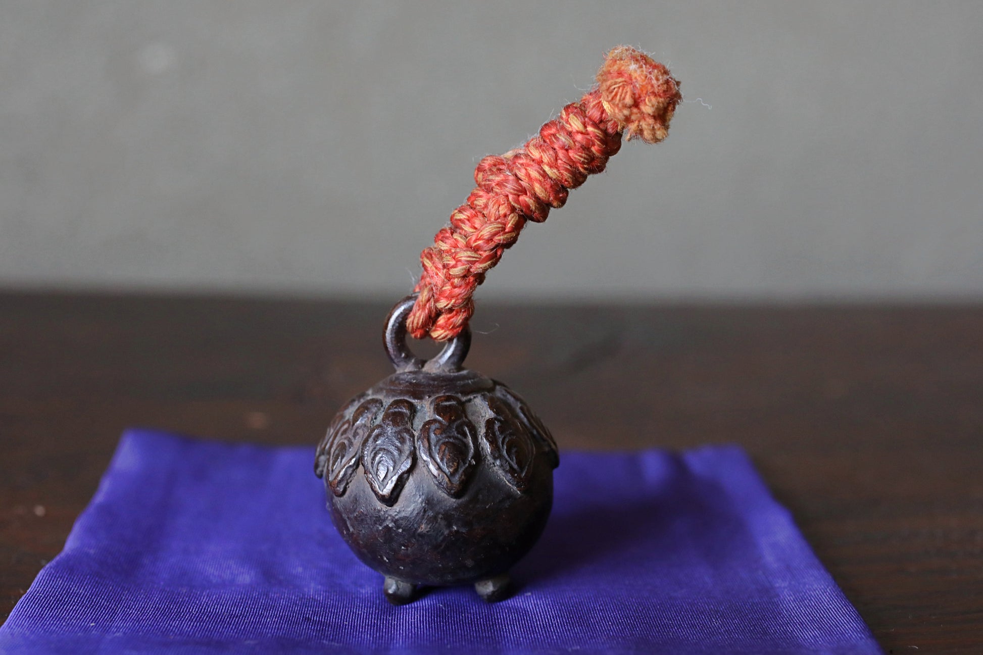 A small, ornate metal bell with a red string attached to it, resting on a blue cloth.