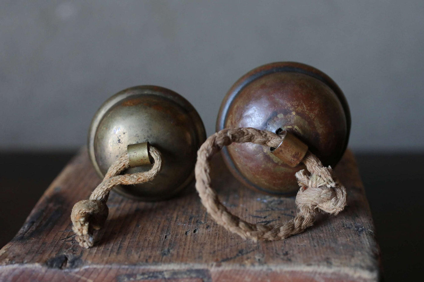 Two brass bells with rope handles are placed on a wooden surface.