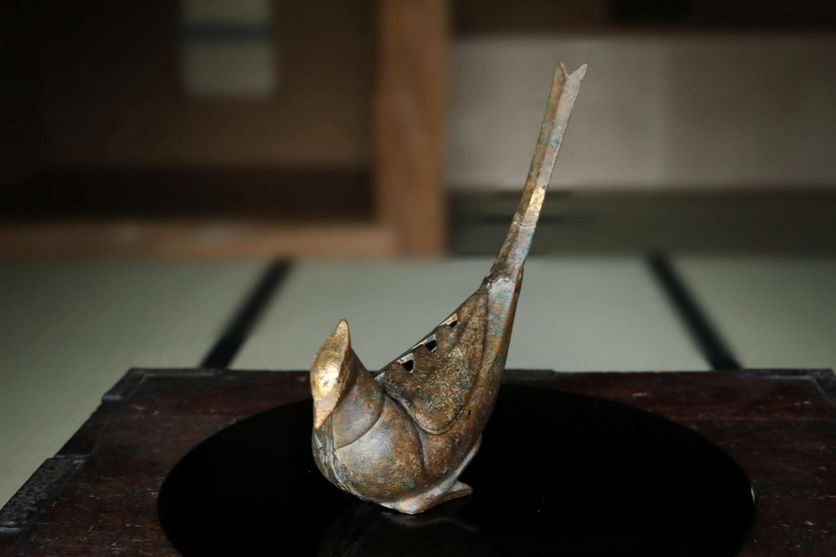 A bronze sculpture of a bird with a long, pointed beak is displayed on a dark surface.