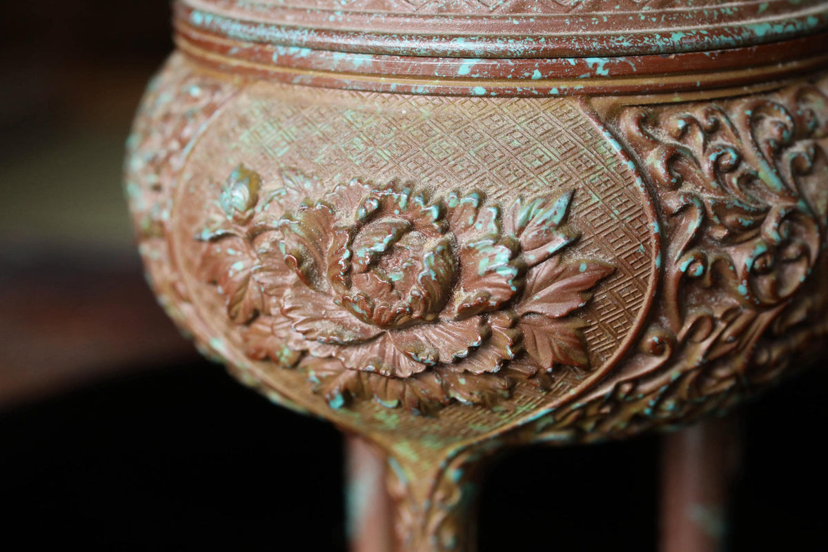 A close-up image of an ornate, antique-looking vase or container with intricate floral designs and patterns.
