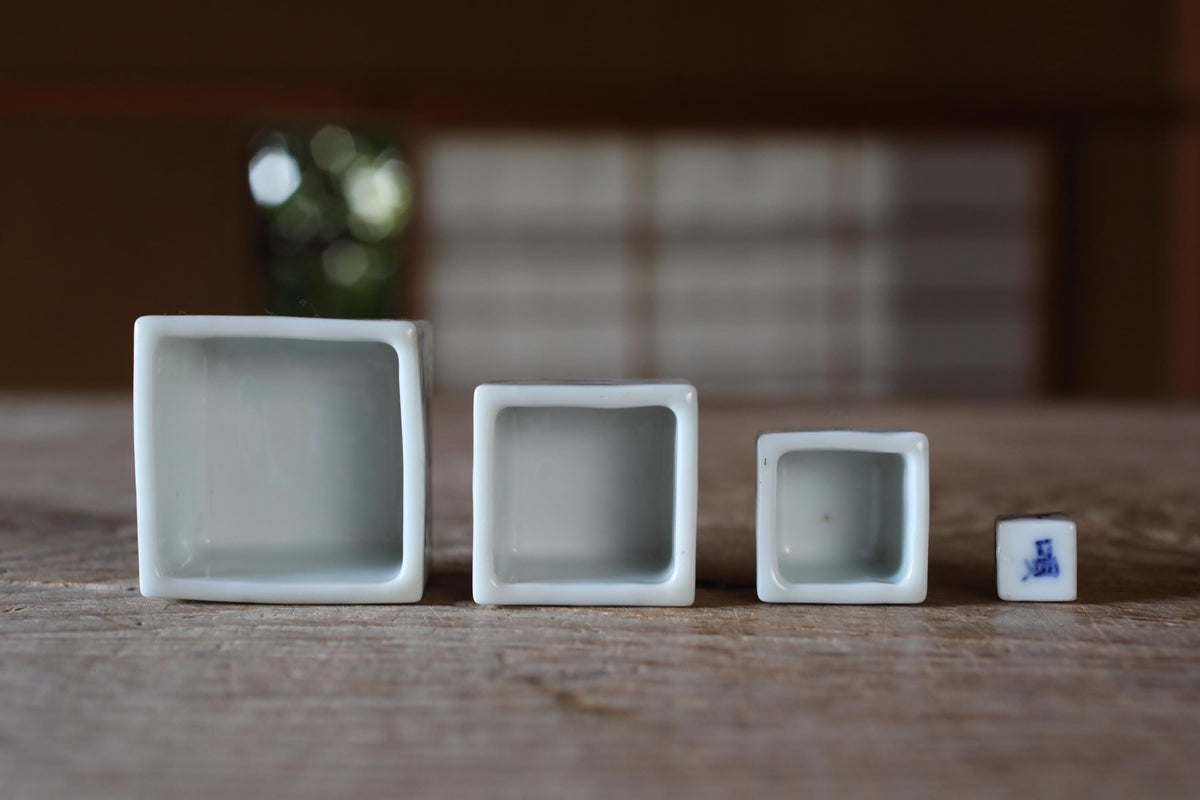 Three white ceramic containers of different sizes are arranged on a wooden surface, with a blurred background.