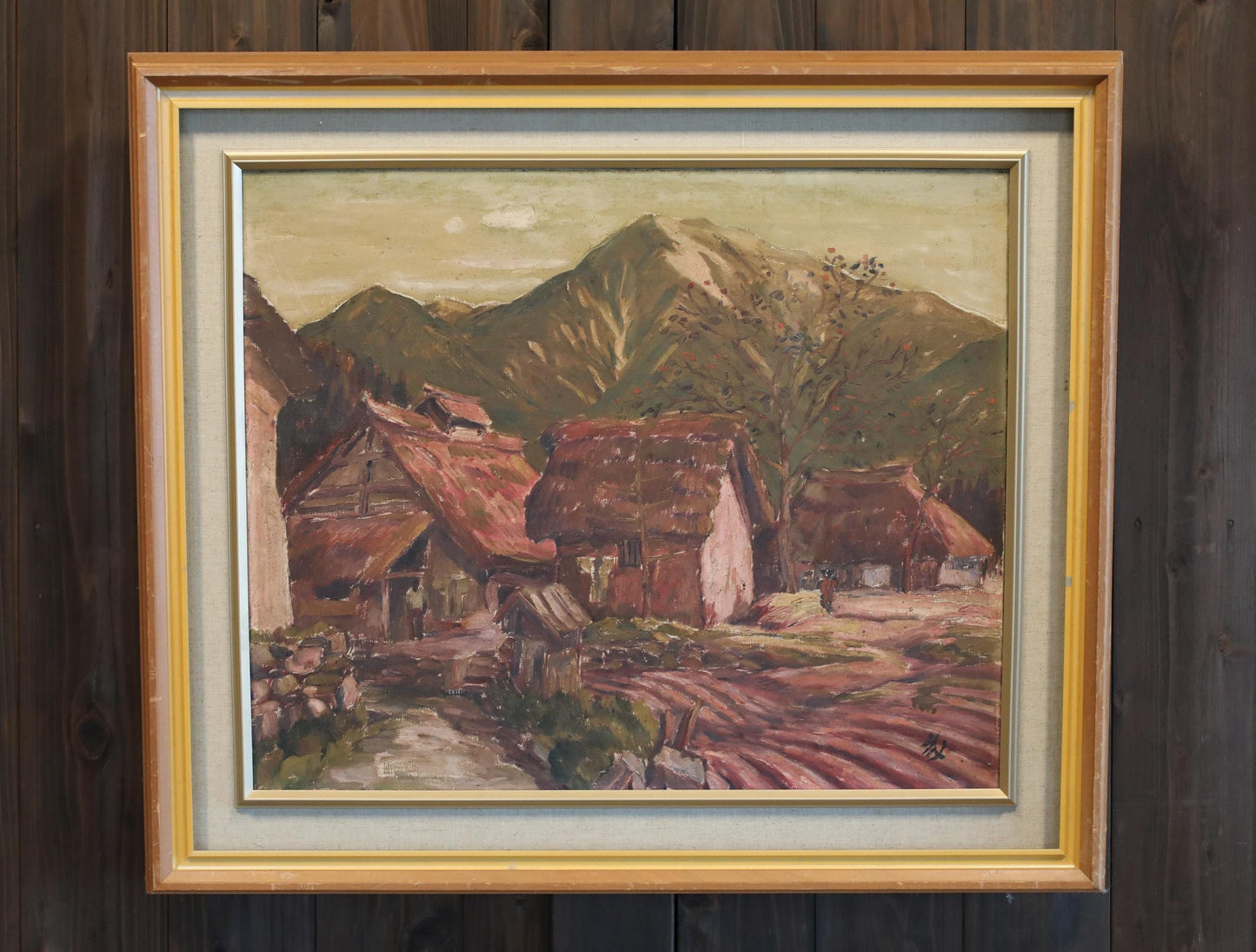 The image is a framed painting depicting a rural landscape with a village, mountains in the background, and a dirt road leading to the village.