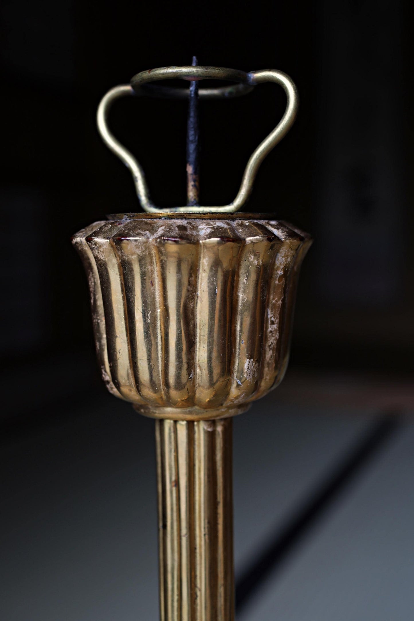 A close-up view of a decorative golden candlestick holder with a curved top and a small spout.