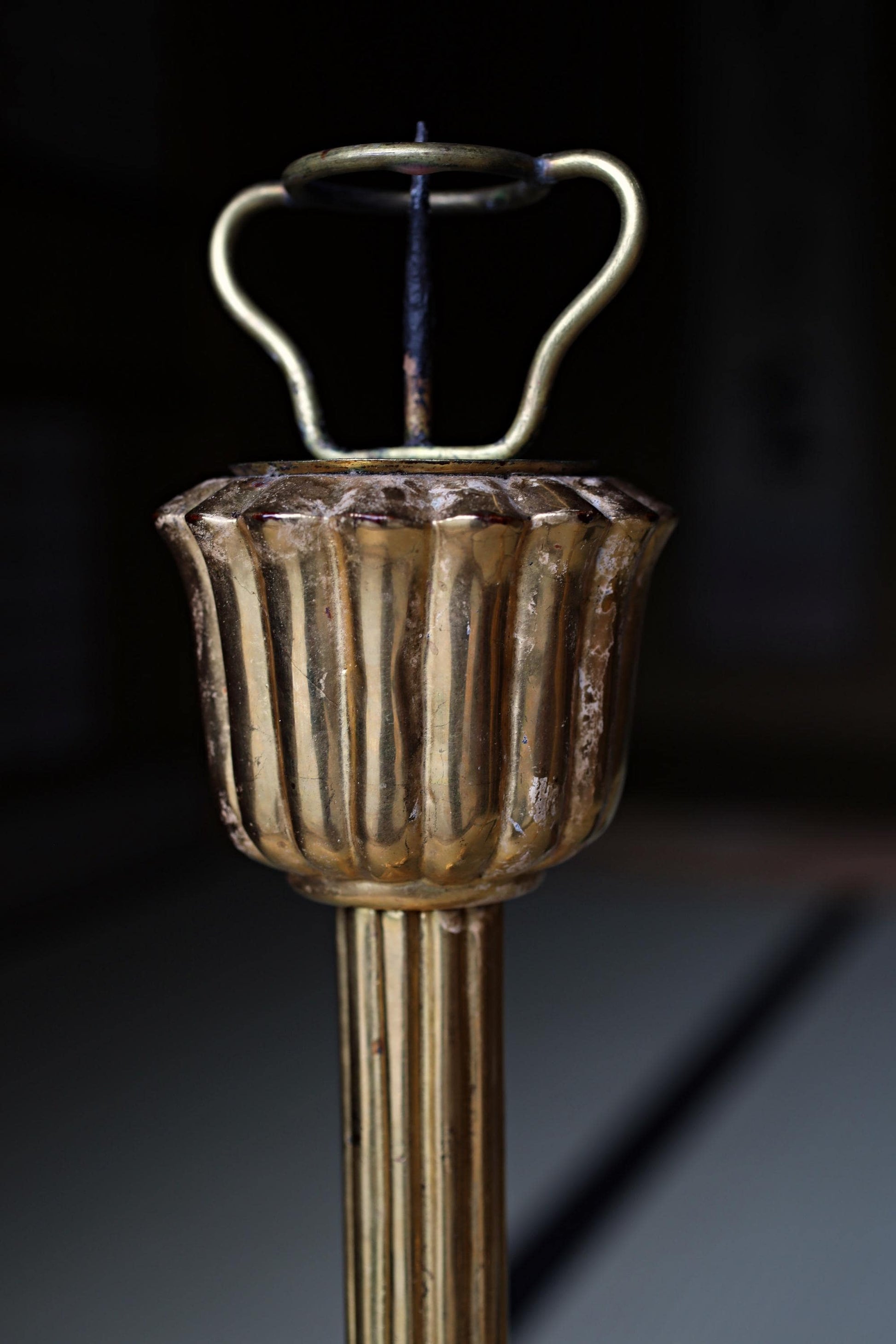 A close-up view of a decorative golden candlestick holder with a curved top and a small spout.