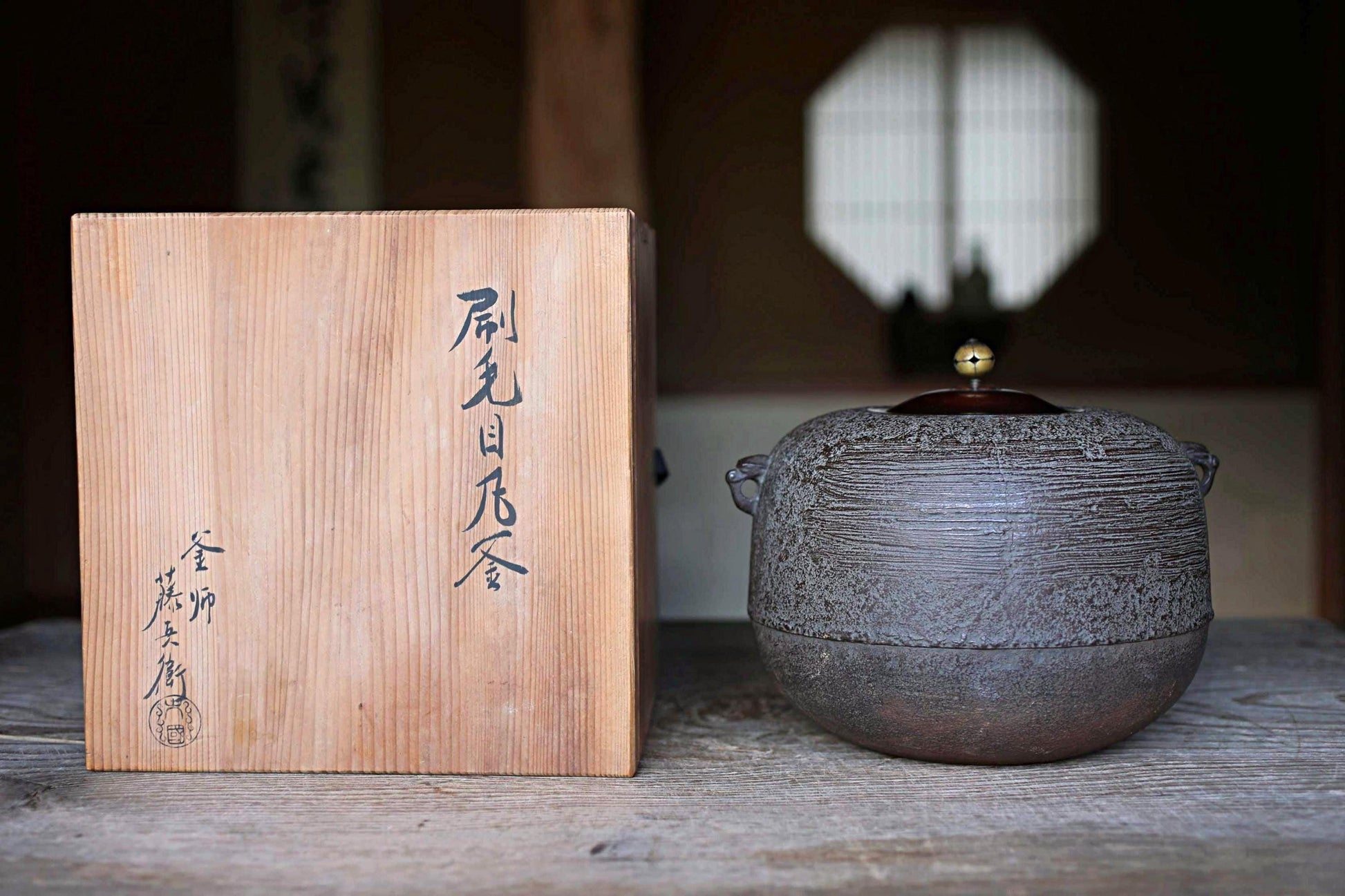 a wooden box with Japanese characters and a ceramic tea pot with a lid, both placed on a wooden surface.
