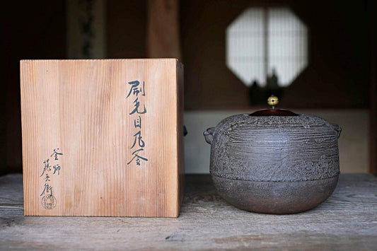 a wooden box with Japanese characters and a ceramic tea pot with a lid, both placed on a wooden surface.