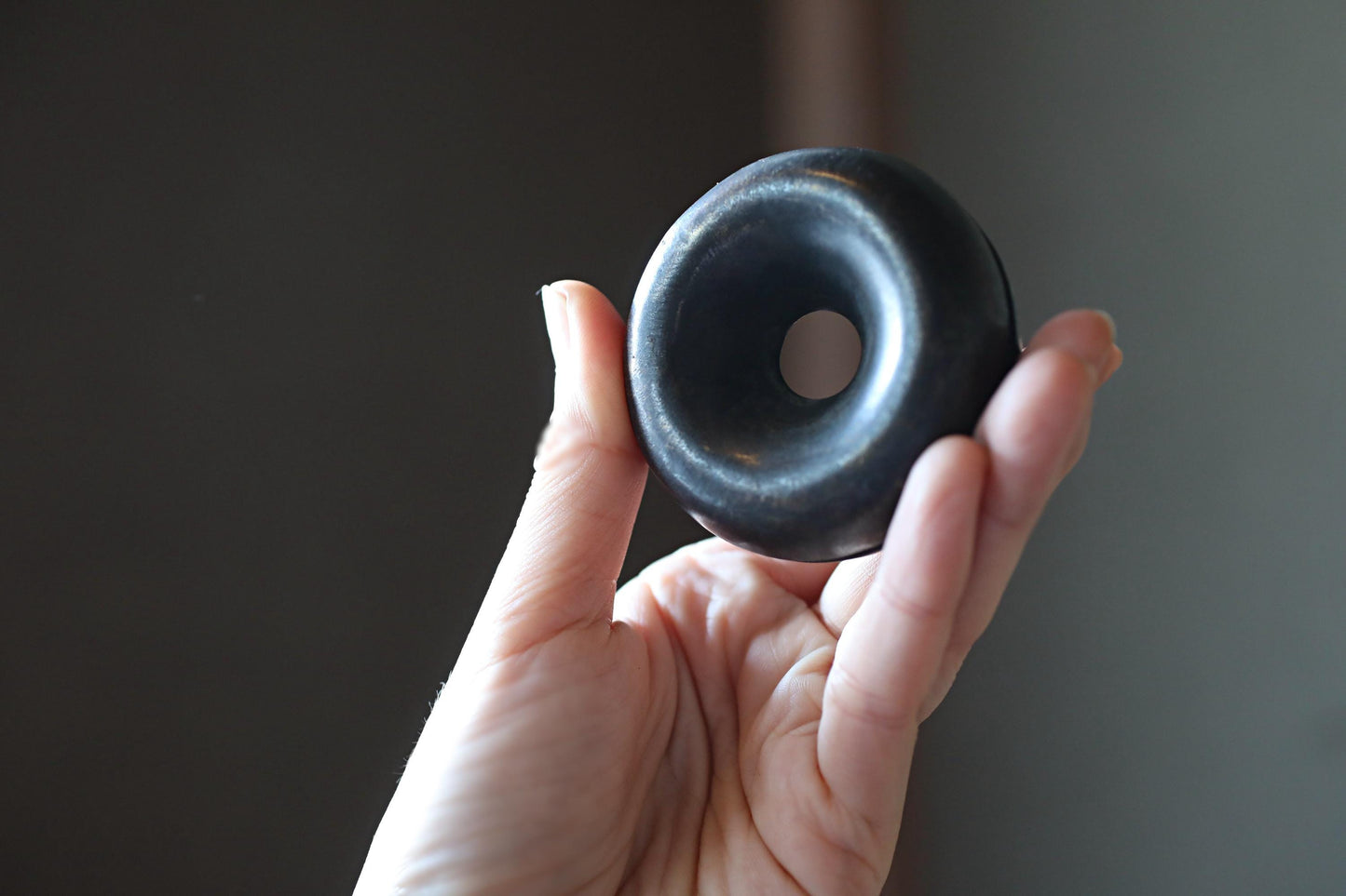 A hand holding a black object with a hole in the center, against a dark background.