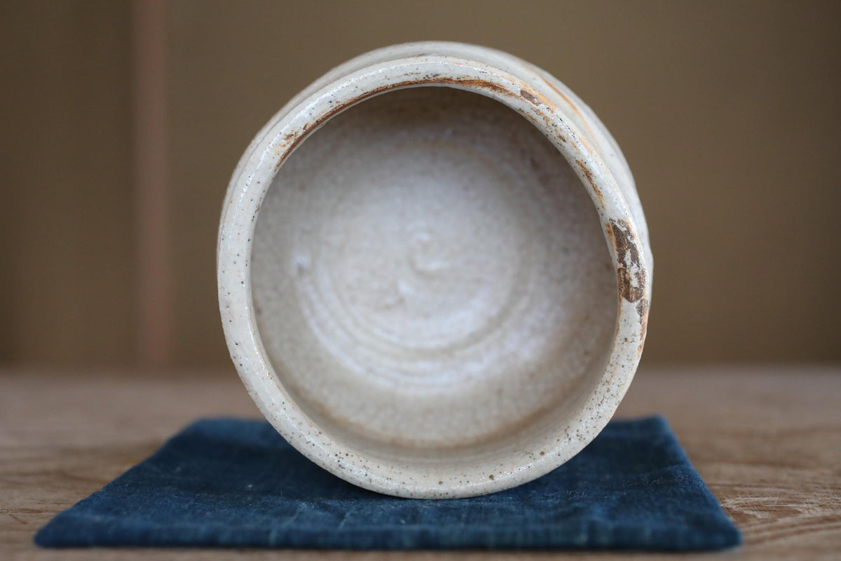 A white ceramic bowl with a speckled texture sits on a blue cloth on a wooden surface.