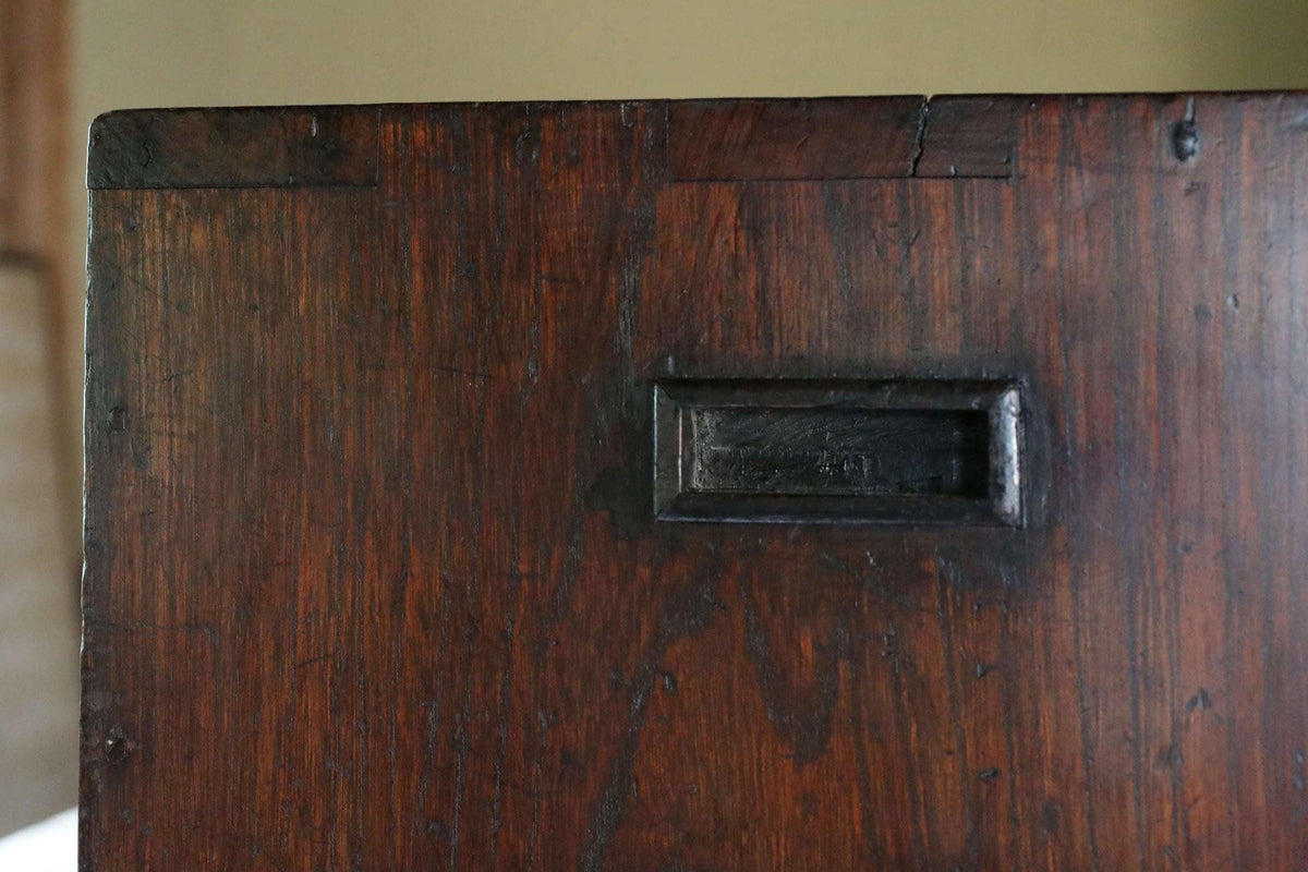 a close-up view of a dark wooden surface with a small rectangular metal object, possibly a drawer or a drawer handle, embedded in it.