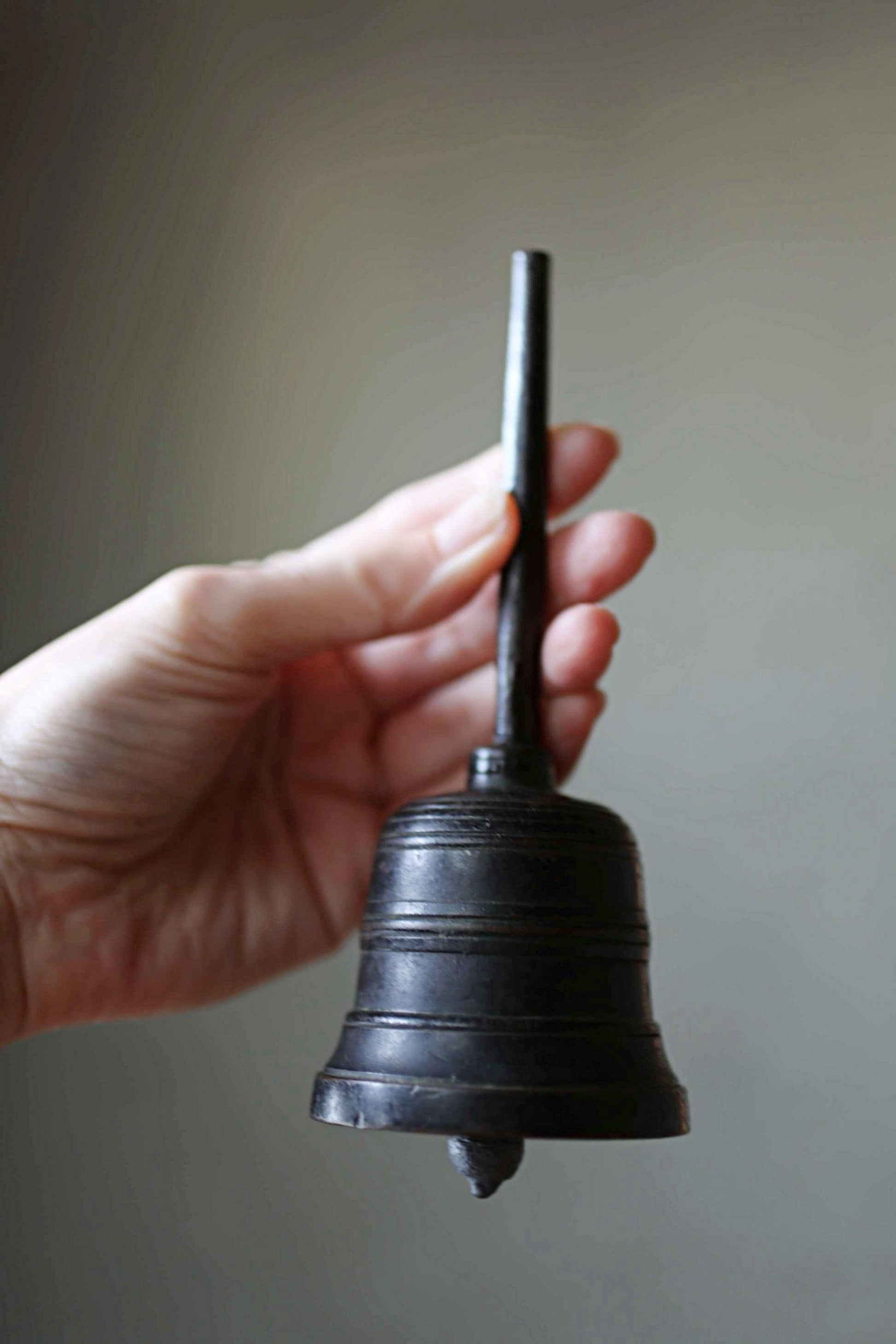 A hand holding a black metal bell with a pointed end.