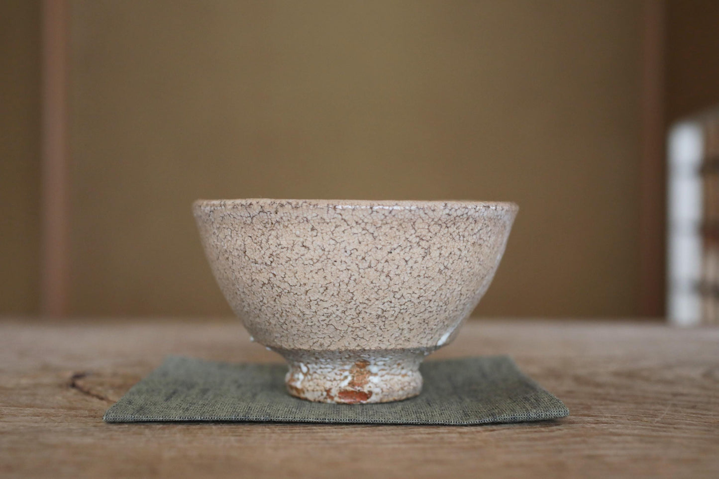 A white ceramic bowl with a speckled texture sits on a green cloth on a wooden surface.