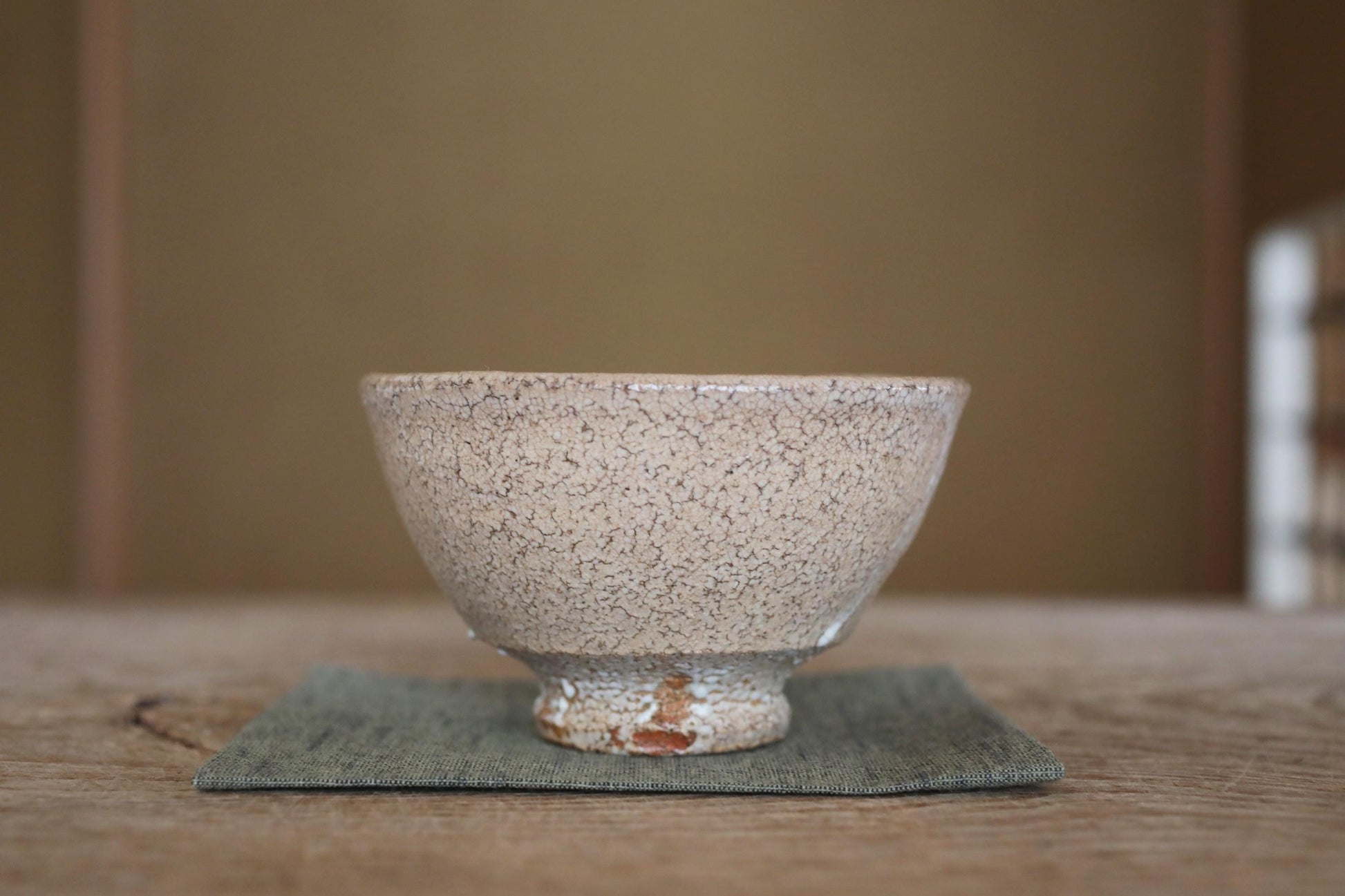 A white ceramic bowl with a speckled texture sits on a green cloth on a wooden surface.