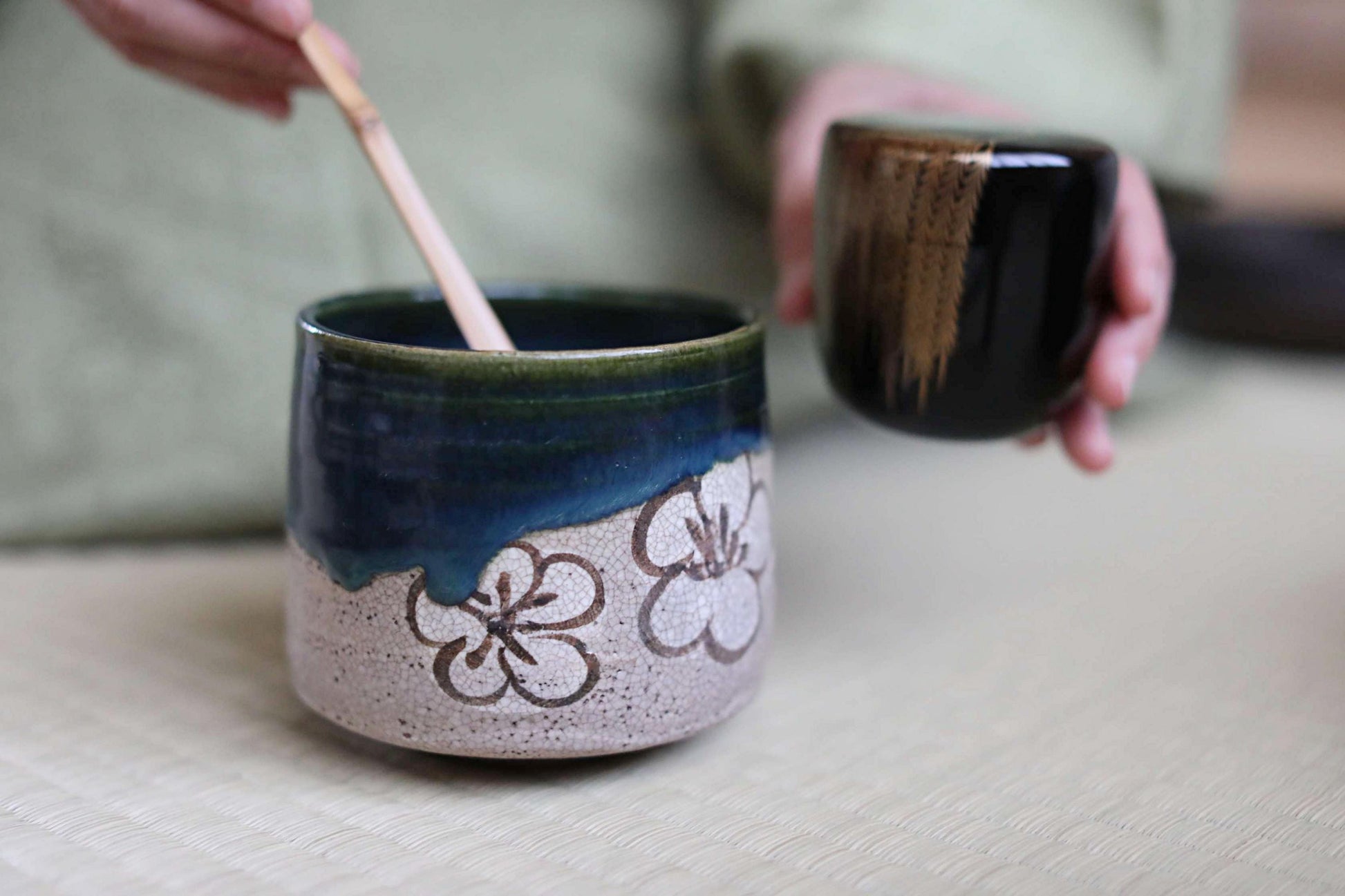 A person's hand is holding a black cup with a floral design, while another cup with a blue and white floral pattern is also visible on the table.