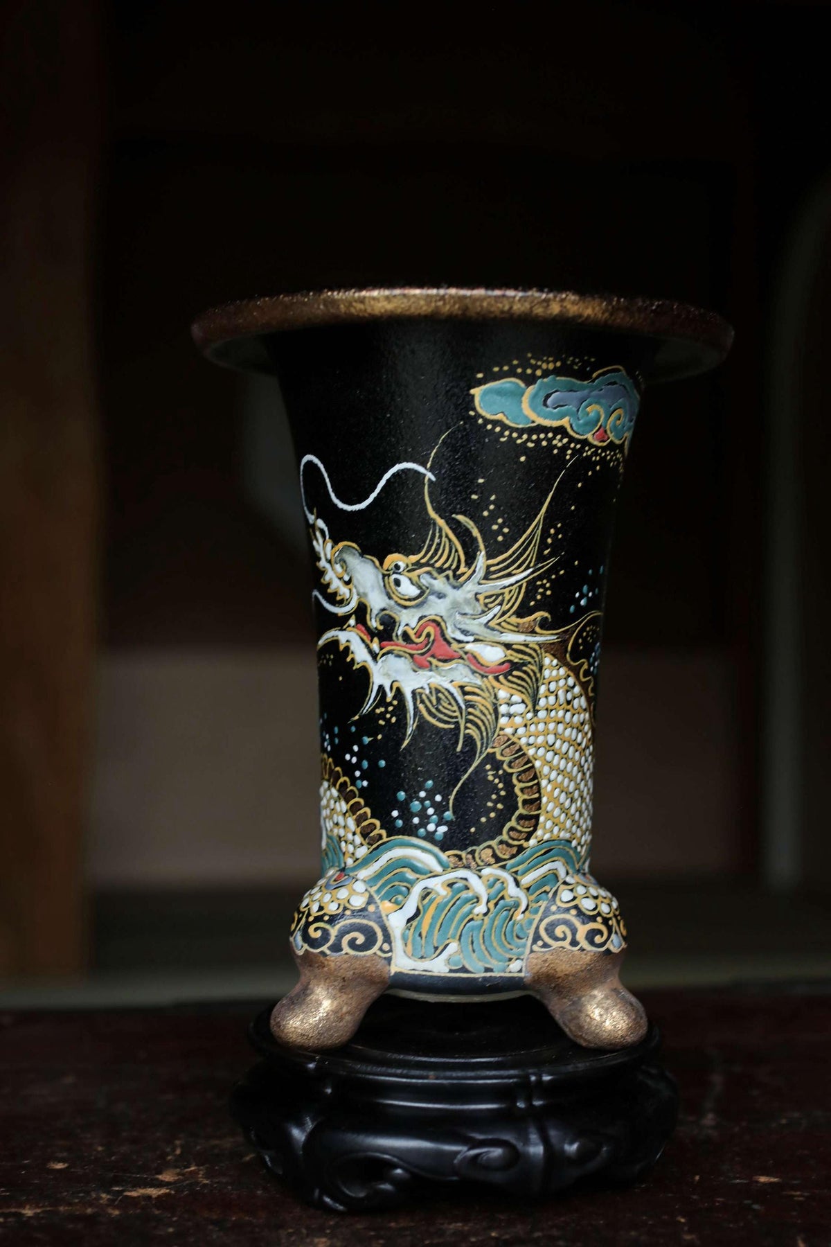 A decorative vase with a dragon design on it, placed on a black stand.