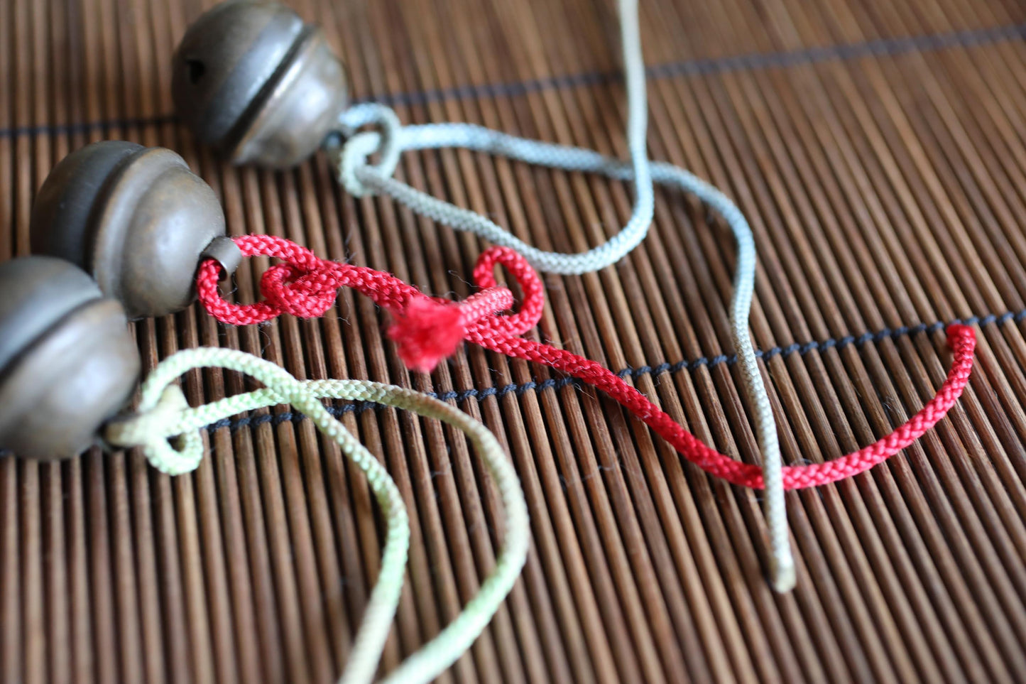 a close-up view of a wooden surface with three metal bells and three strings, one of which is red.