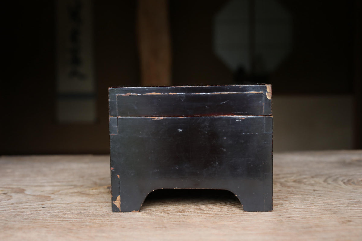 A black, rectangular box sits on a wooden surface, with a blurred background.