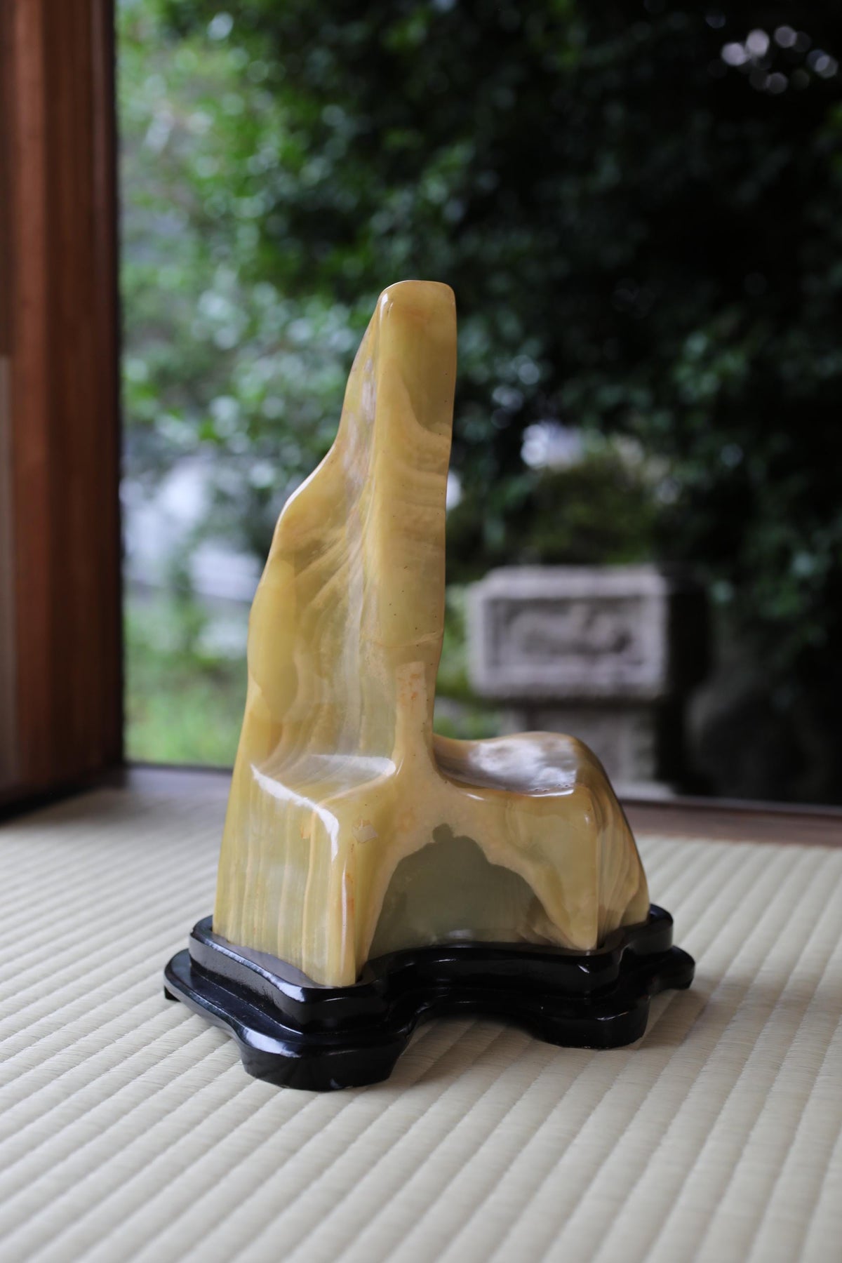 a yellow stone sculpture with a unique, organic shape, sitting on a black base and placed on a wooden surface.