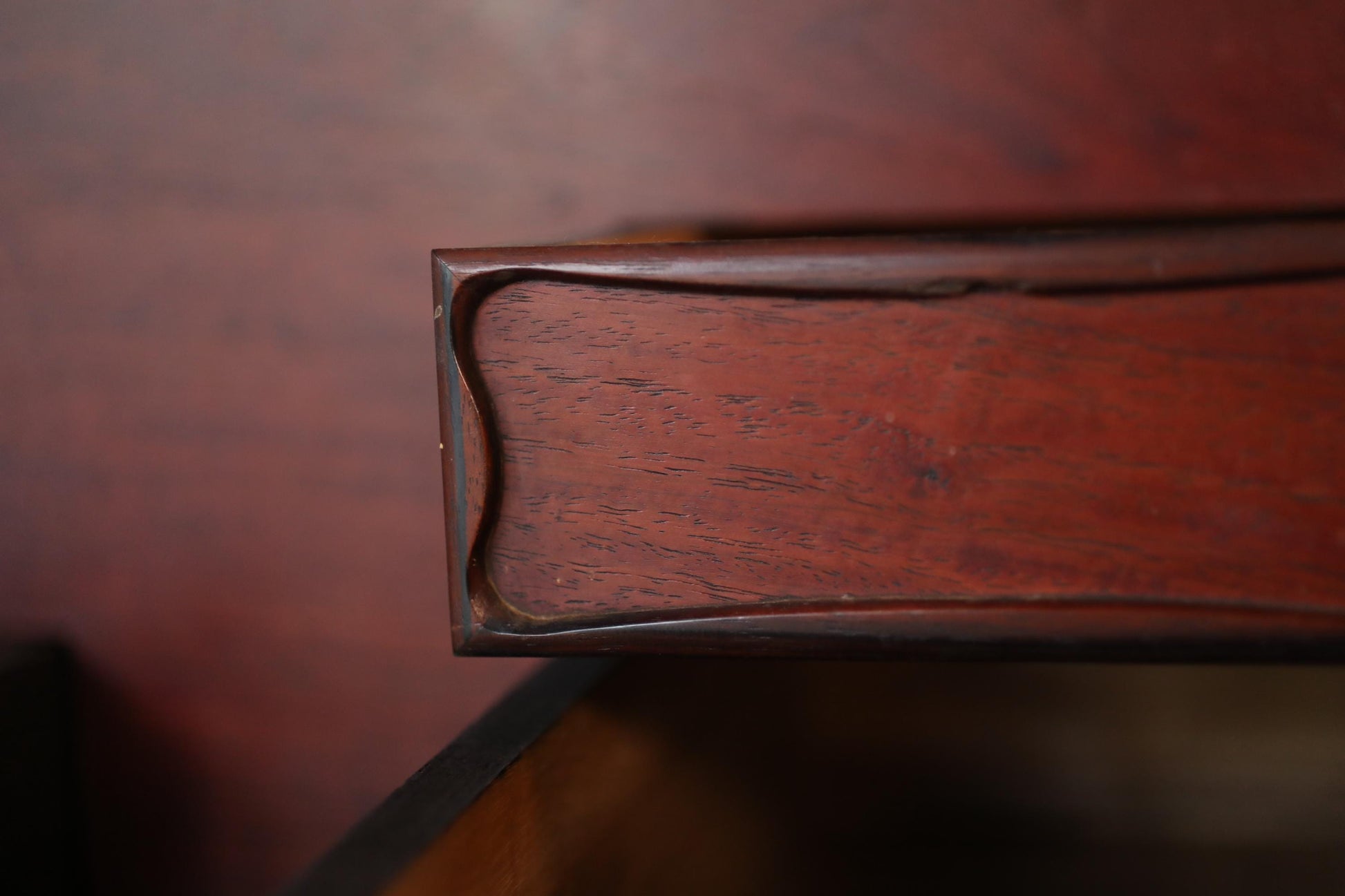 A close-up view of a wooden drawer or cabinet, with a rich, dark brown finish. The grain and texture of the wood are visible, creating a sense of depth and dimension in the image.