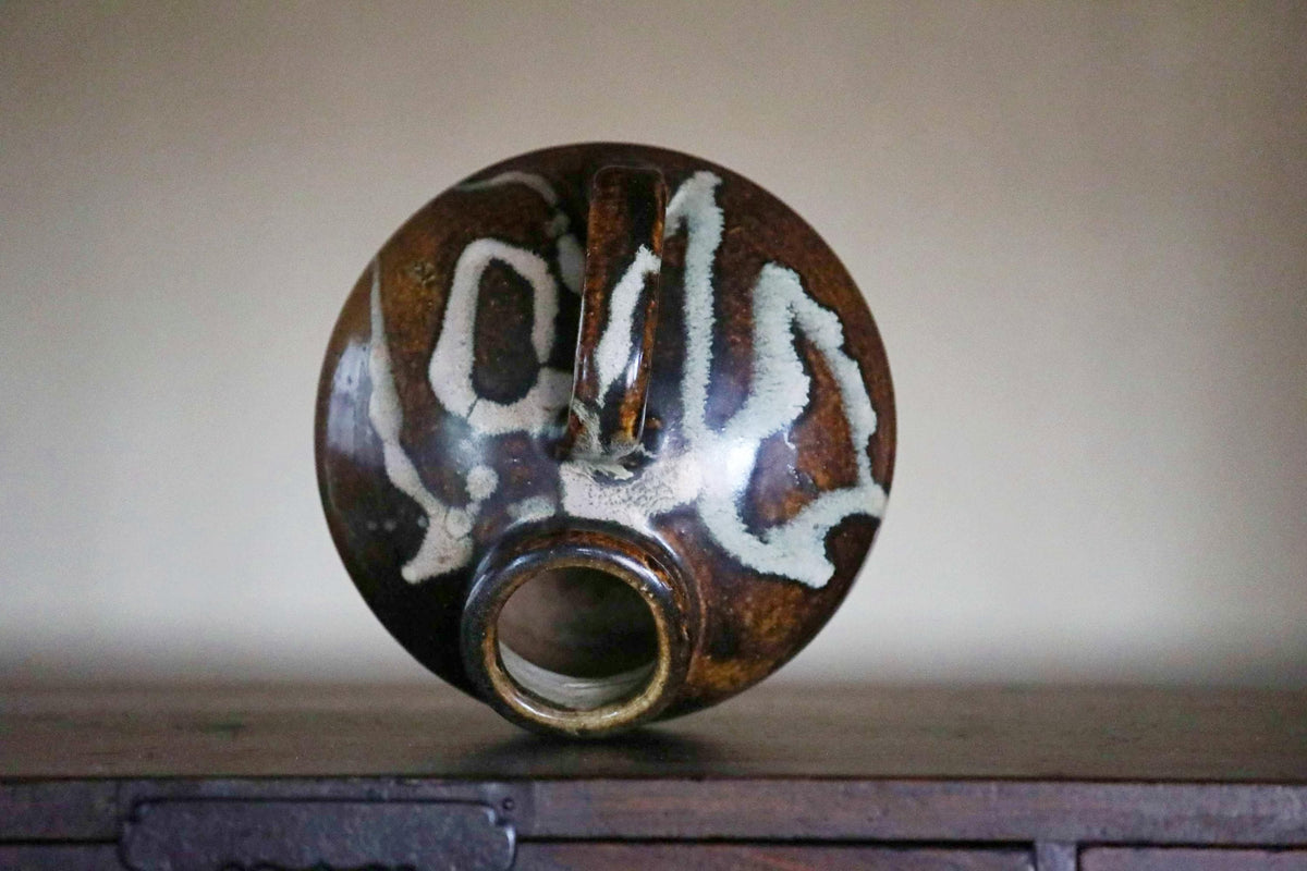 A brown and white ceramic vase with a unique design sits on a wooden surface.