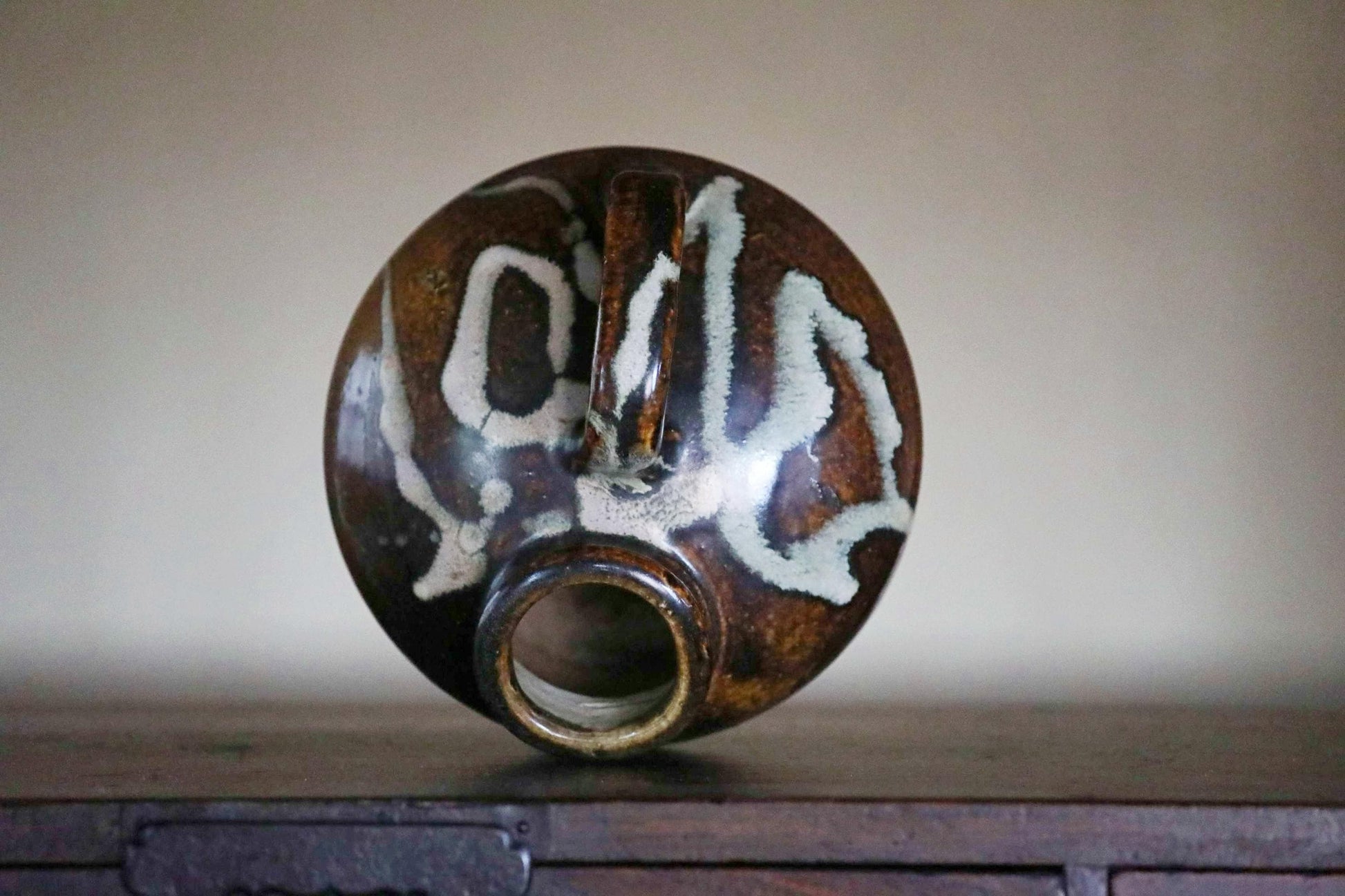 A brown and white ceramic vase with a unique design sits on a wooden surface.